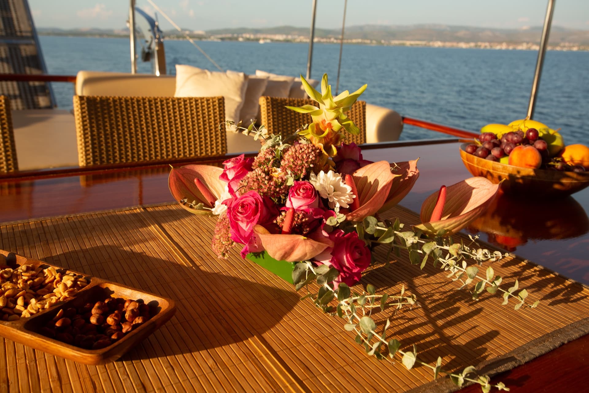 Flower arrangement and snacks on a yacht table overlooking the sea and distant coastline.