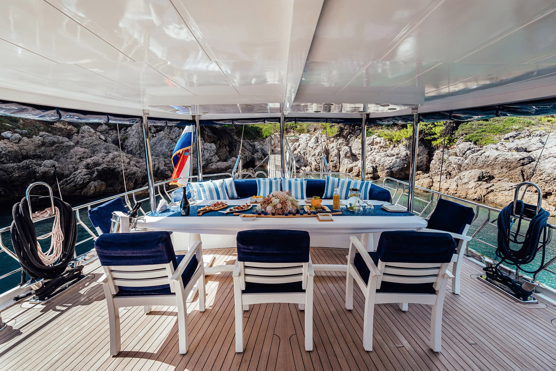 Yacht dining area with prepared food, set against rocky coastline and turquoise water