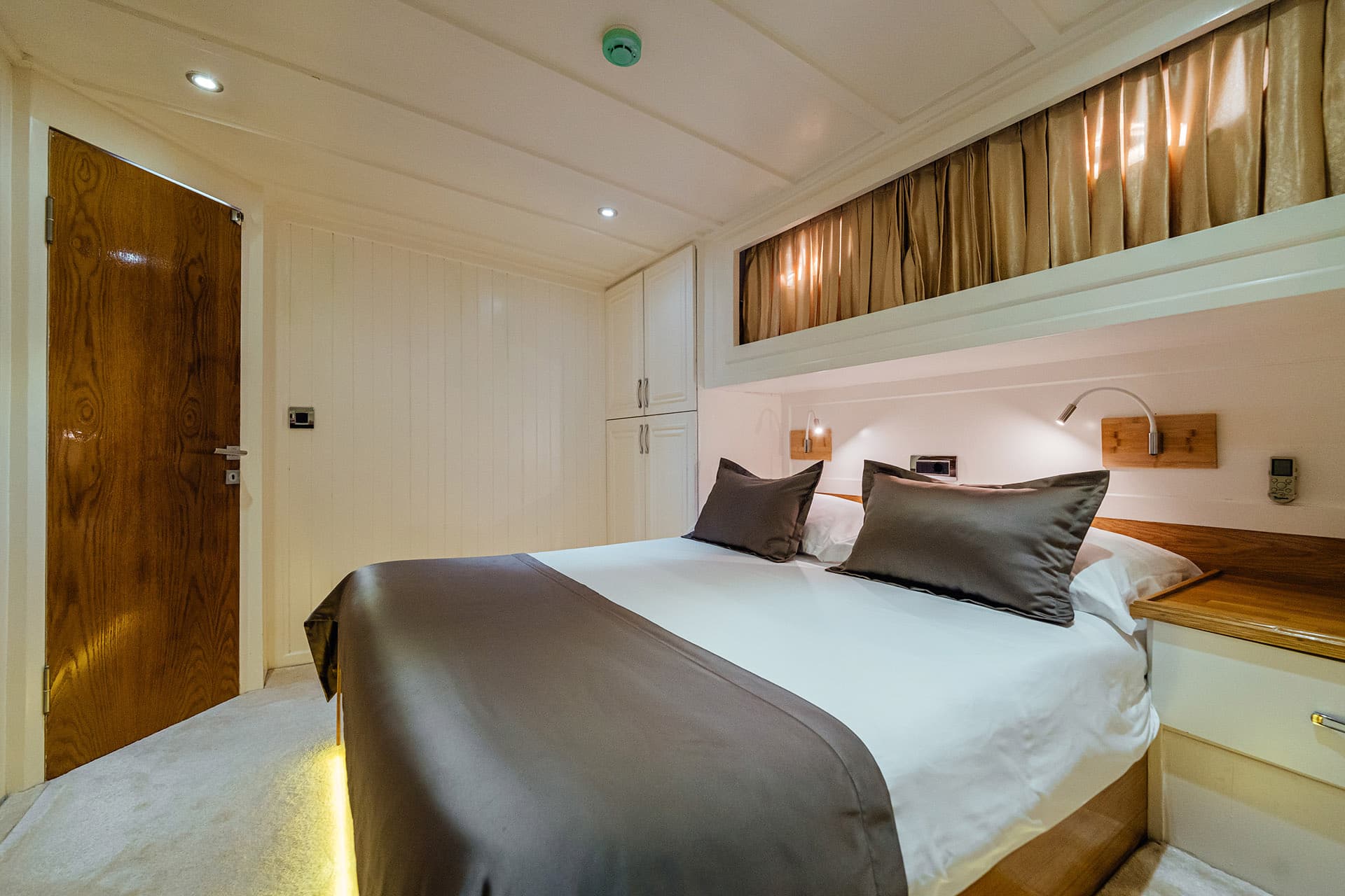 Double cabin bedroom with white walls, wood accents, and a made bed on a boat.