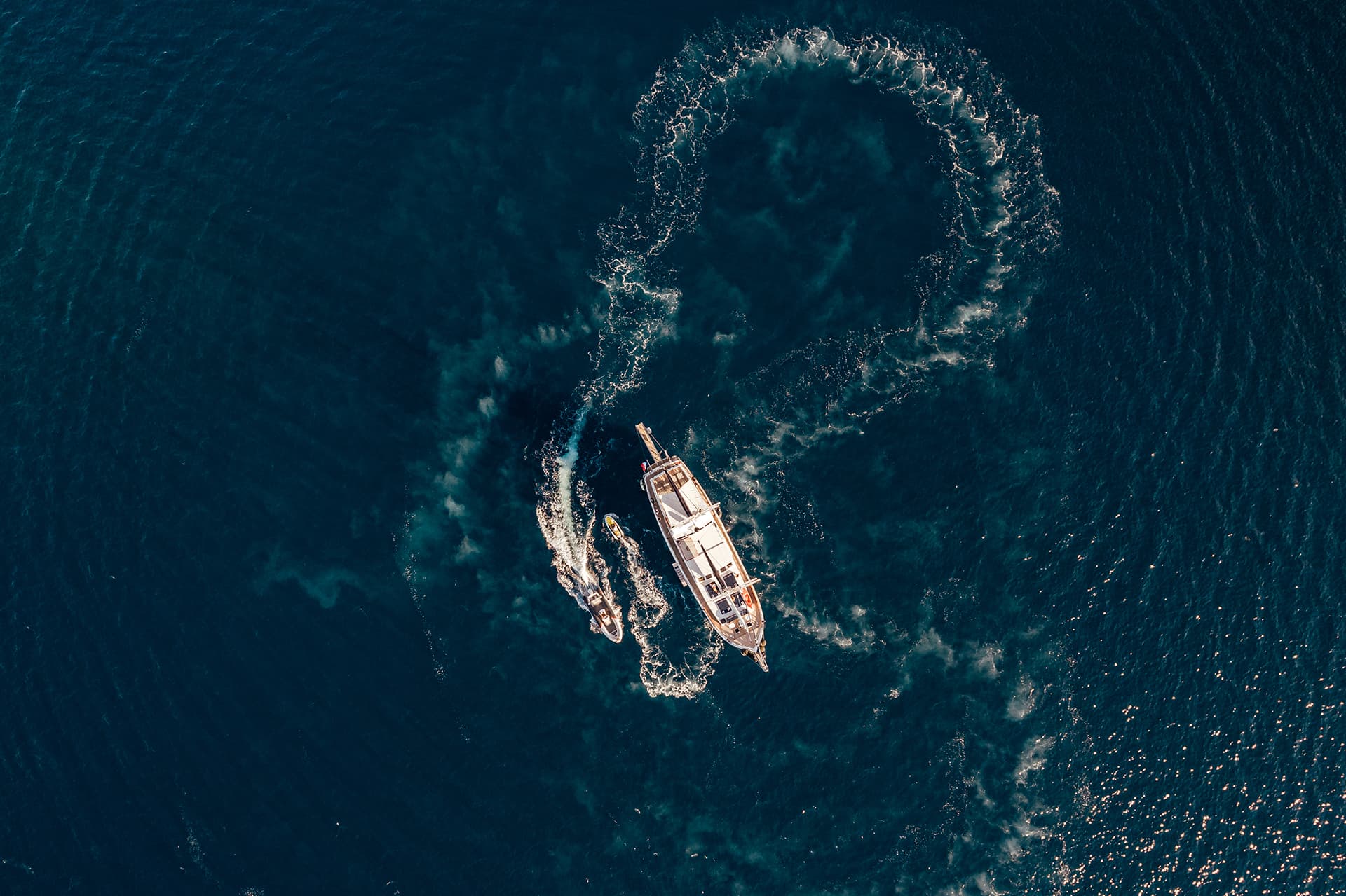 Aerial view of a wooden gulet boat and a small tender boat on deep blue sea water.
