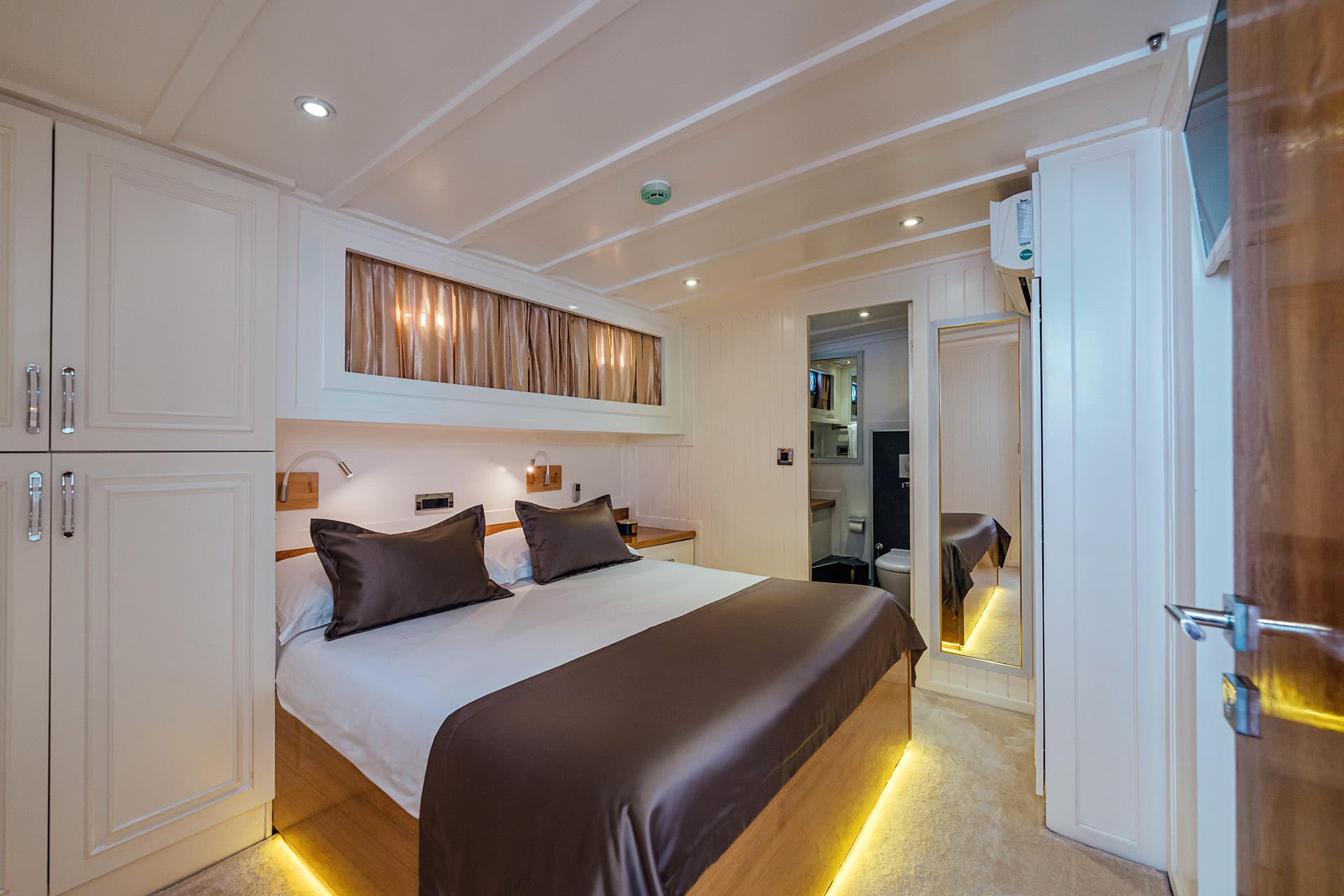 Cabin bedroom with white paneling, double bed, and illuminated wood base on a gulet boat.