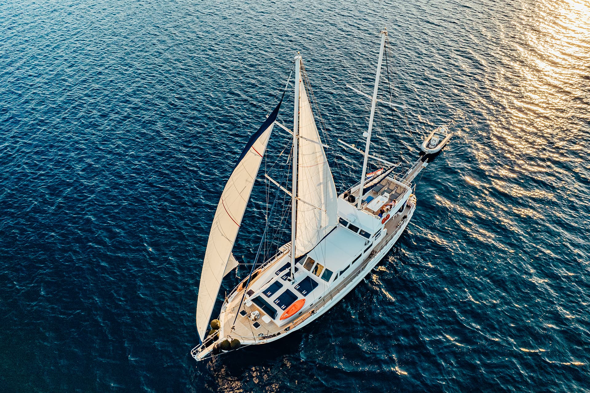 Gulet sailboat with sails up on deep blue water at sunset, aerial view