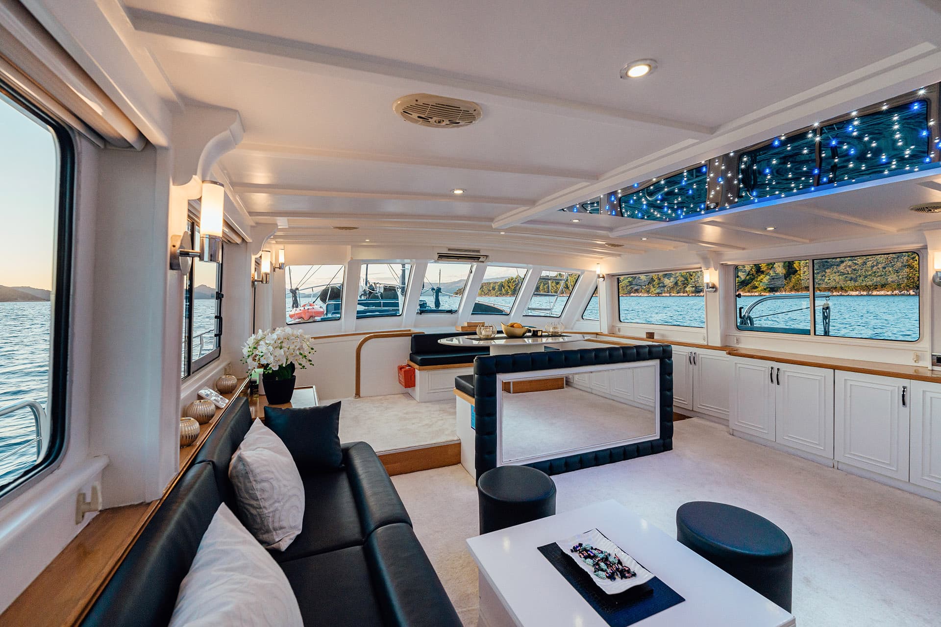 Interior salon of a gulet yacht with sea views, white cabinetry, and blue ceiling lights.