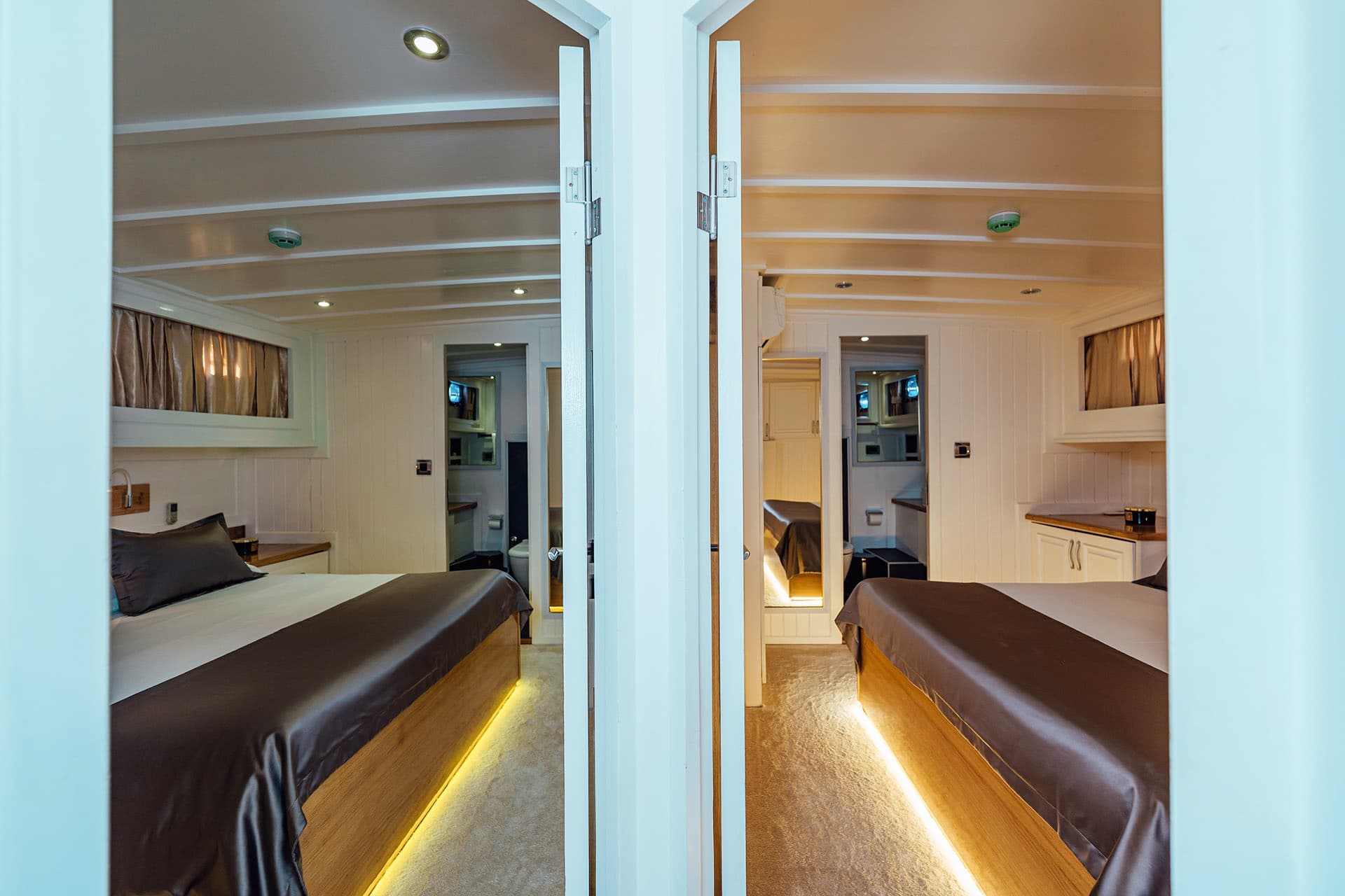 Twin cabin interior on a Gulet boat with modern white paneling and illuminated wooden beds.