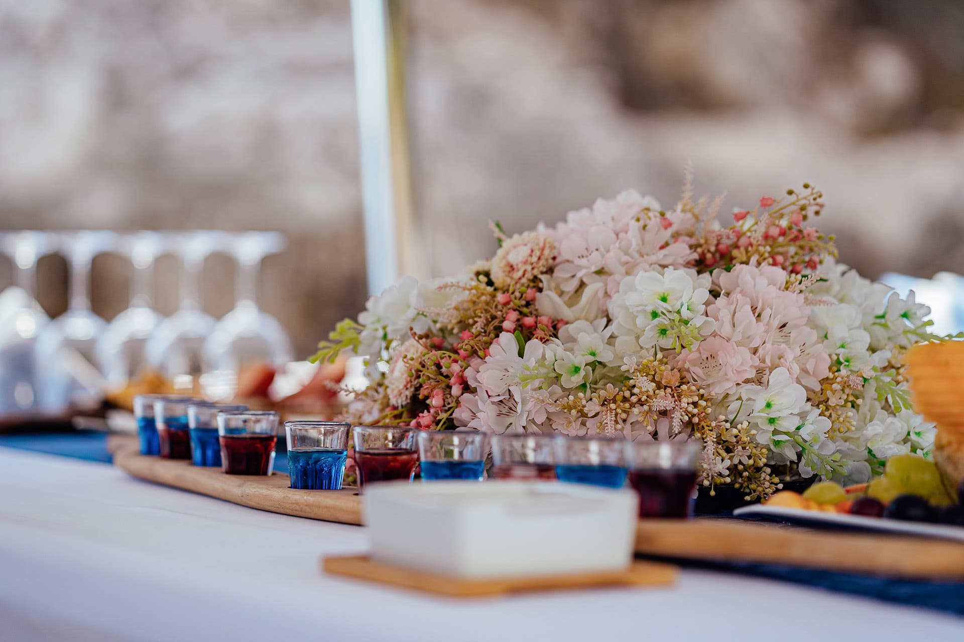 Shot glasses with blue and red drinks, floral centerpiece, and wine glasses on a table setting.
