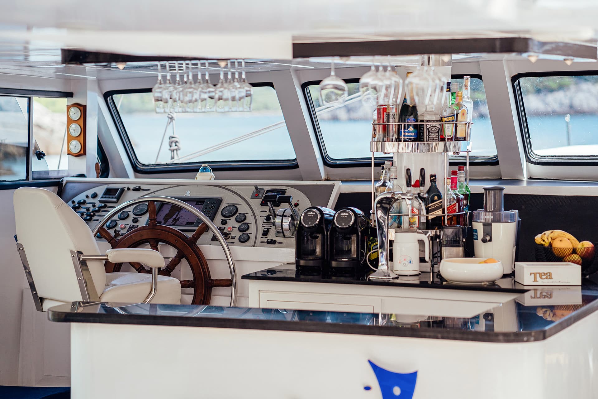 Boat helm station with bar setup, glassware, and view of blue water.