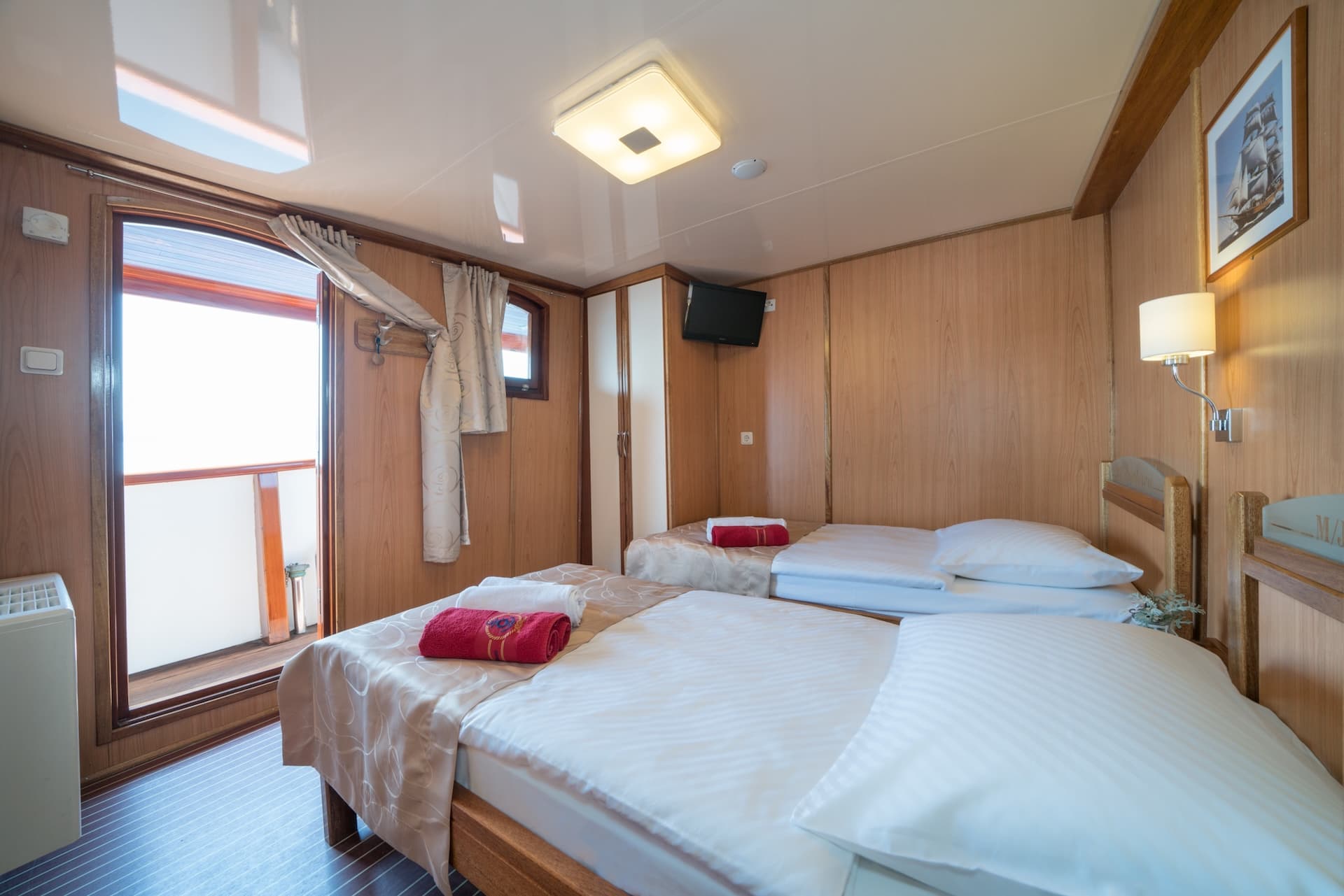 Twin cabin interior with wood paneling, white bedding, and open door leading to bright exterior.