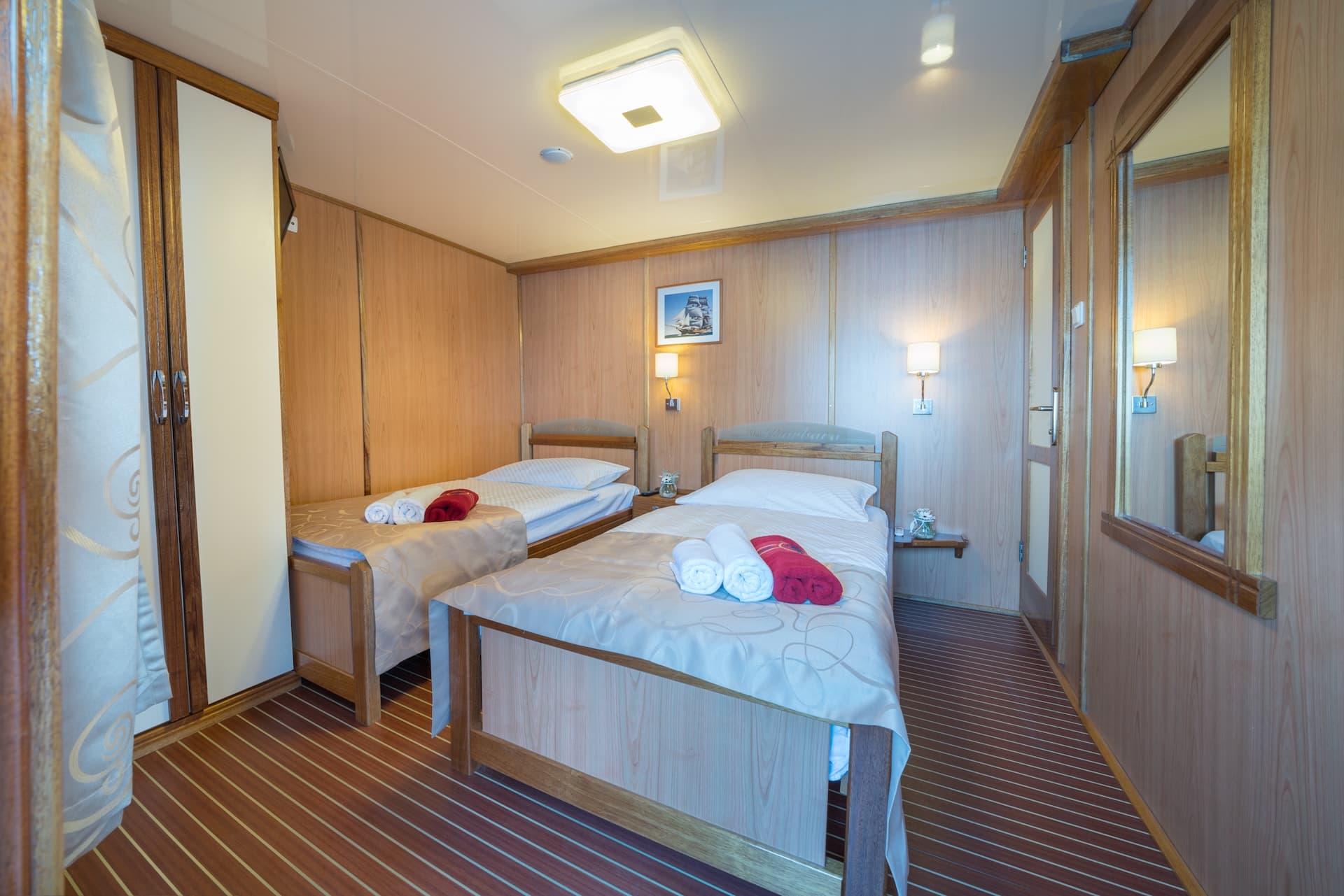 Twin cabin interior with wood paneling, two single beds, and nautical decor on a ship.