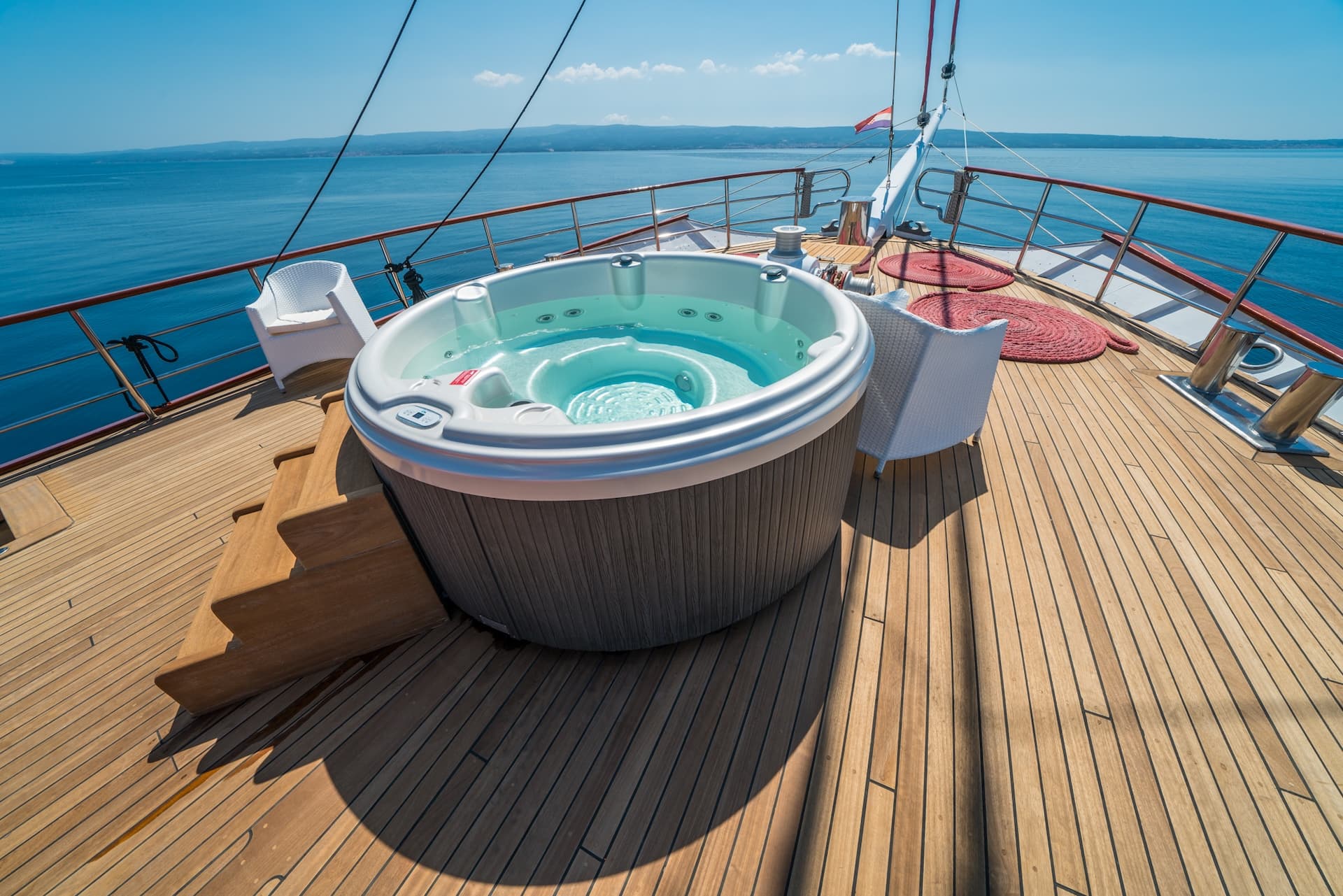 Hot tub on wooden deck of boat sailing on blue sea with distant coastline