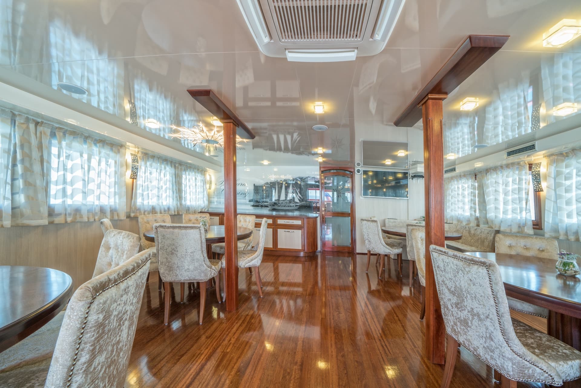 Dining area interior on a boat with wood floors and plush chairs, featuring a mural of a ship.
