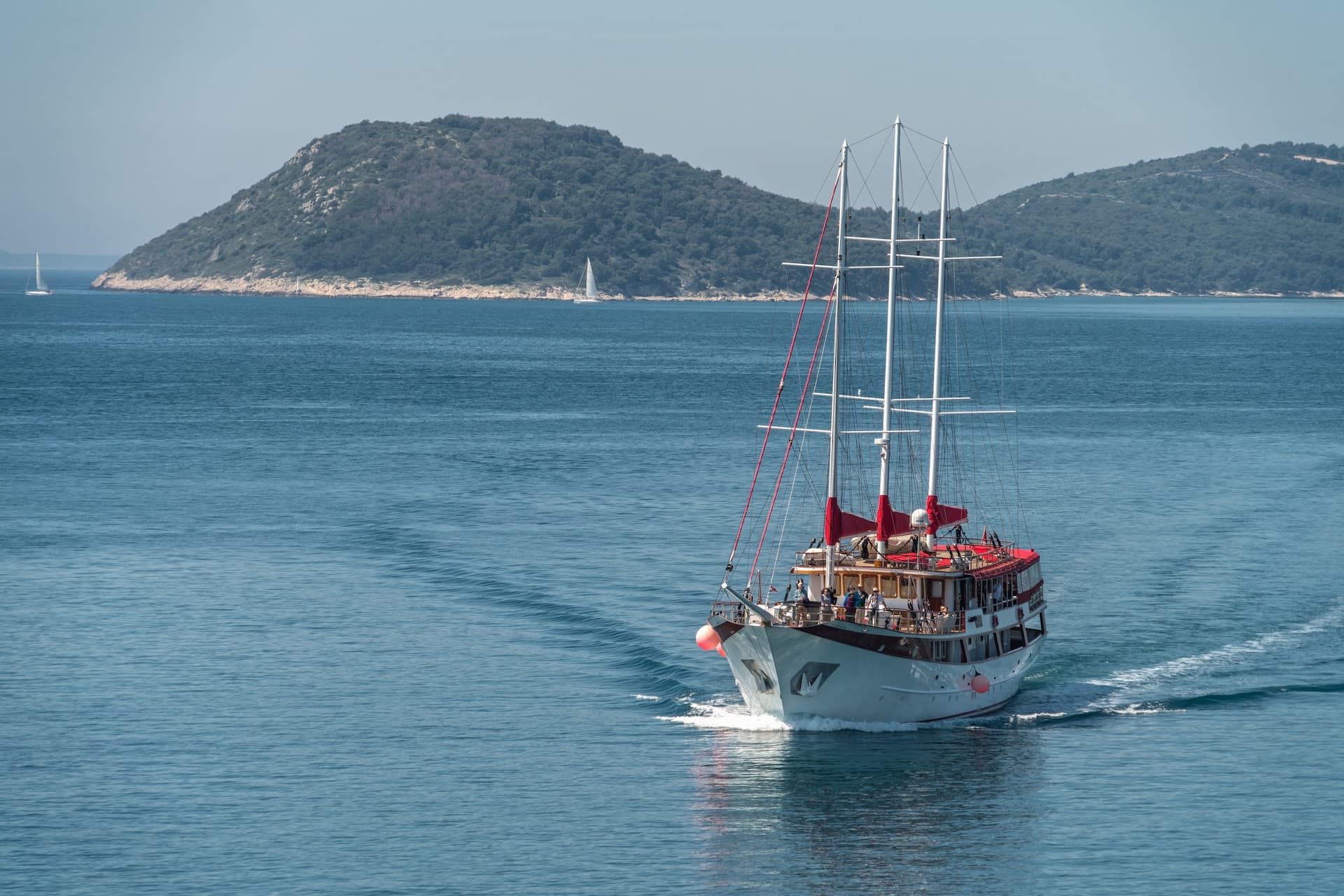 Large sailboat with red accents cruising on blue sea near forested island hills