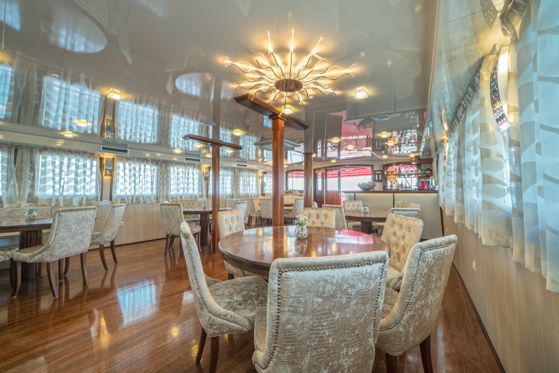 Luxurious dining room interior with polished wood floors and sun-shaped chandelier on a boat.