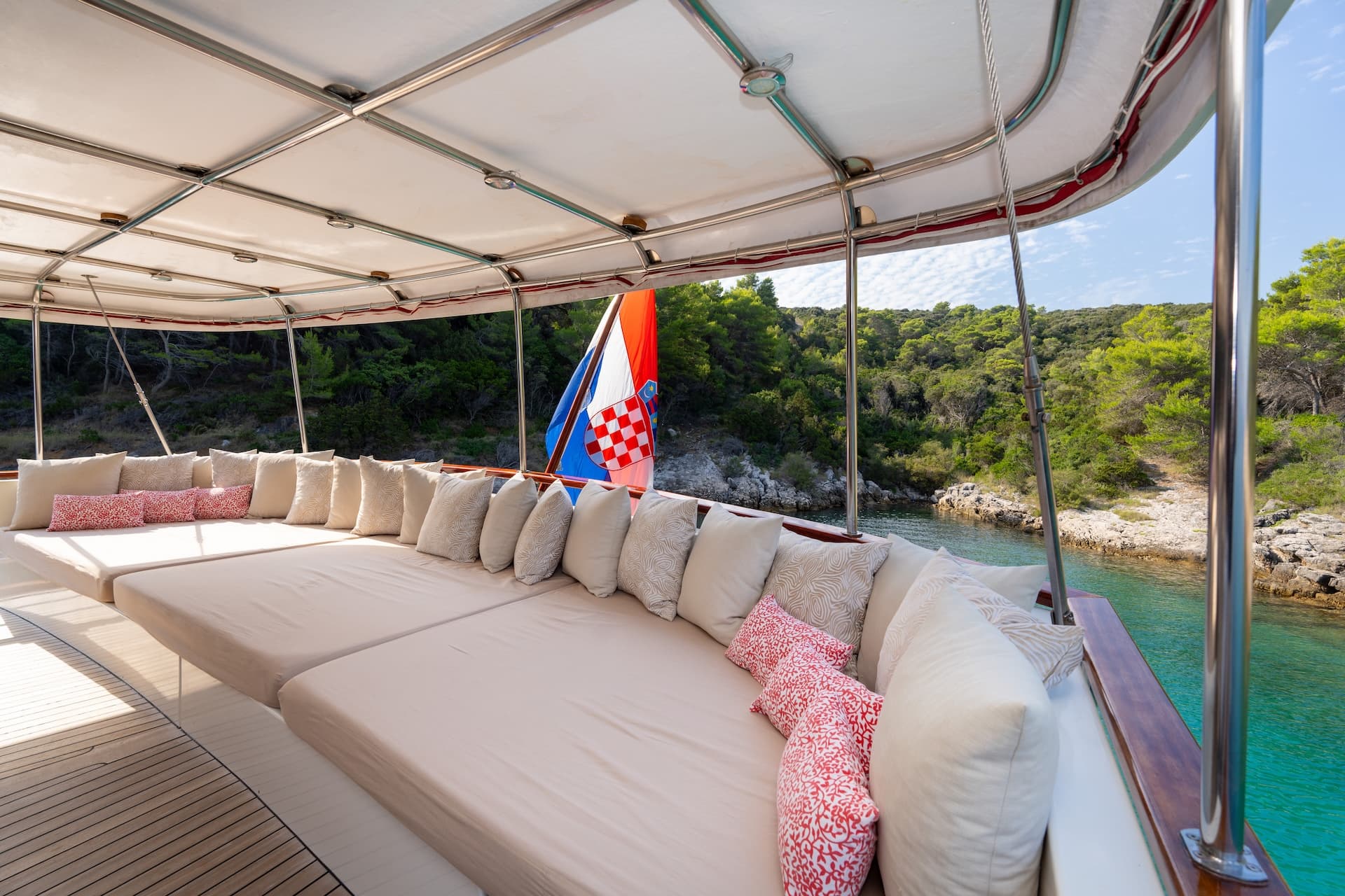 Cosy outdoor sofa with cushions on a gulet overlooking turquoise water and forested coastline.