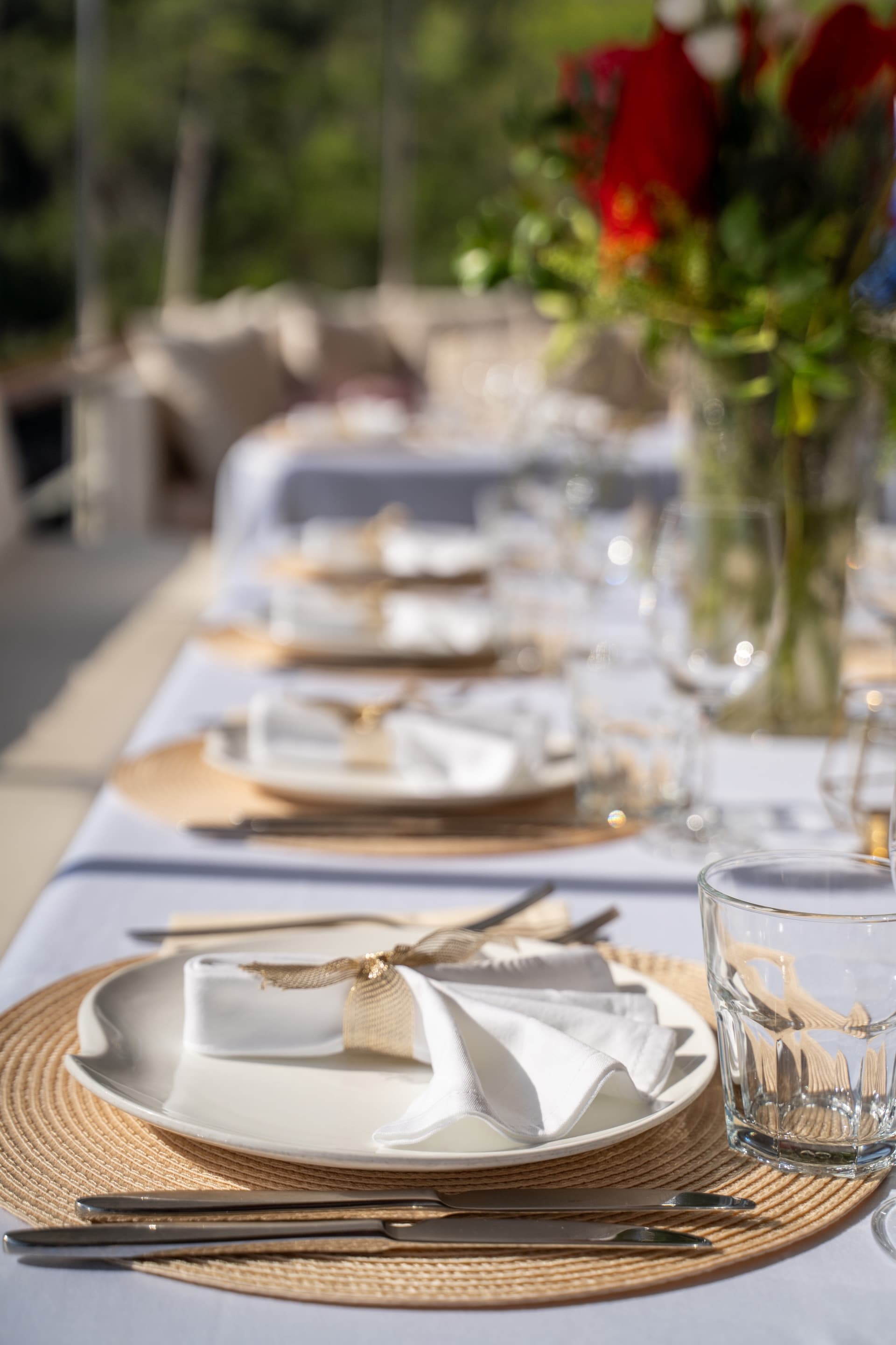 Outdoor dinner table setting on a gulet with white linens, woven placemats, and floral centerpiece.