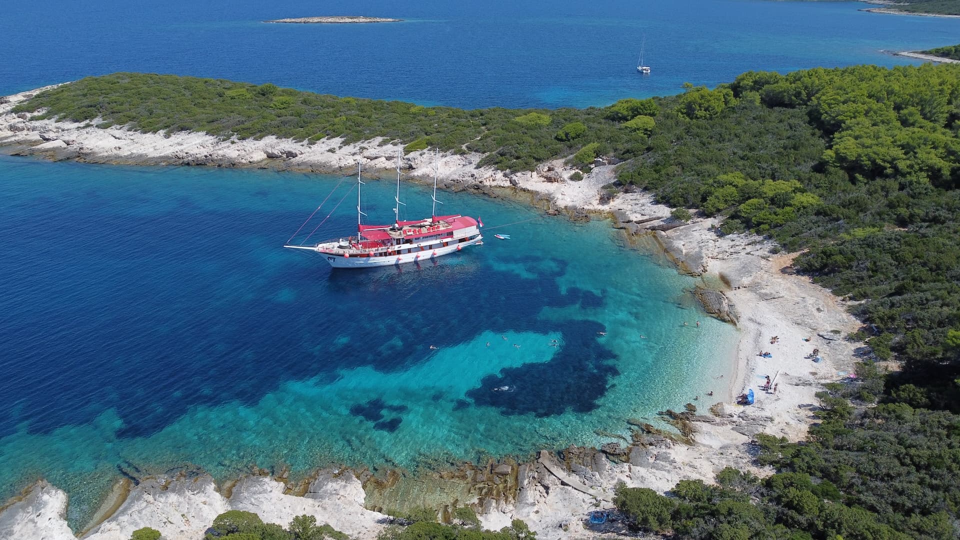 Gulet Barbara boat anchored in turquoise cove near rocky, forested coastline.