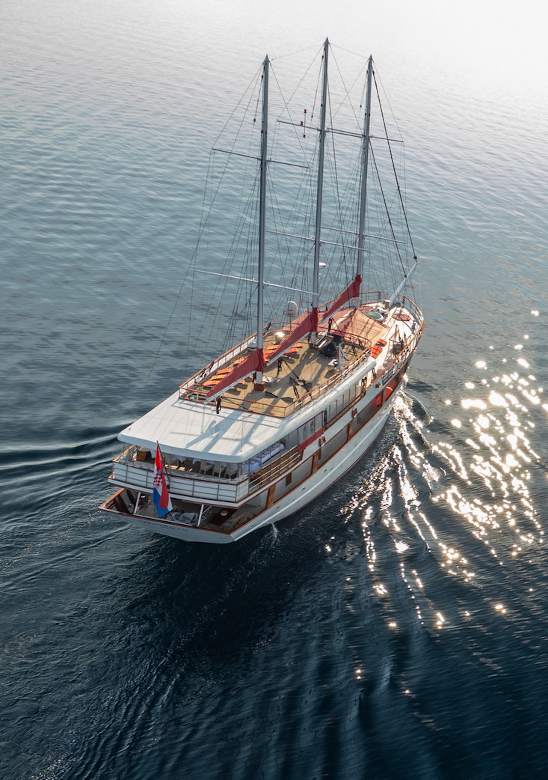 Gulet Barbara sailing on dark blue Adriatic Sea water with sun glare on the surface.