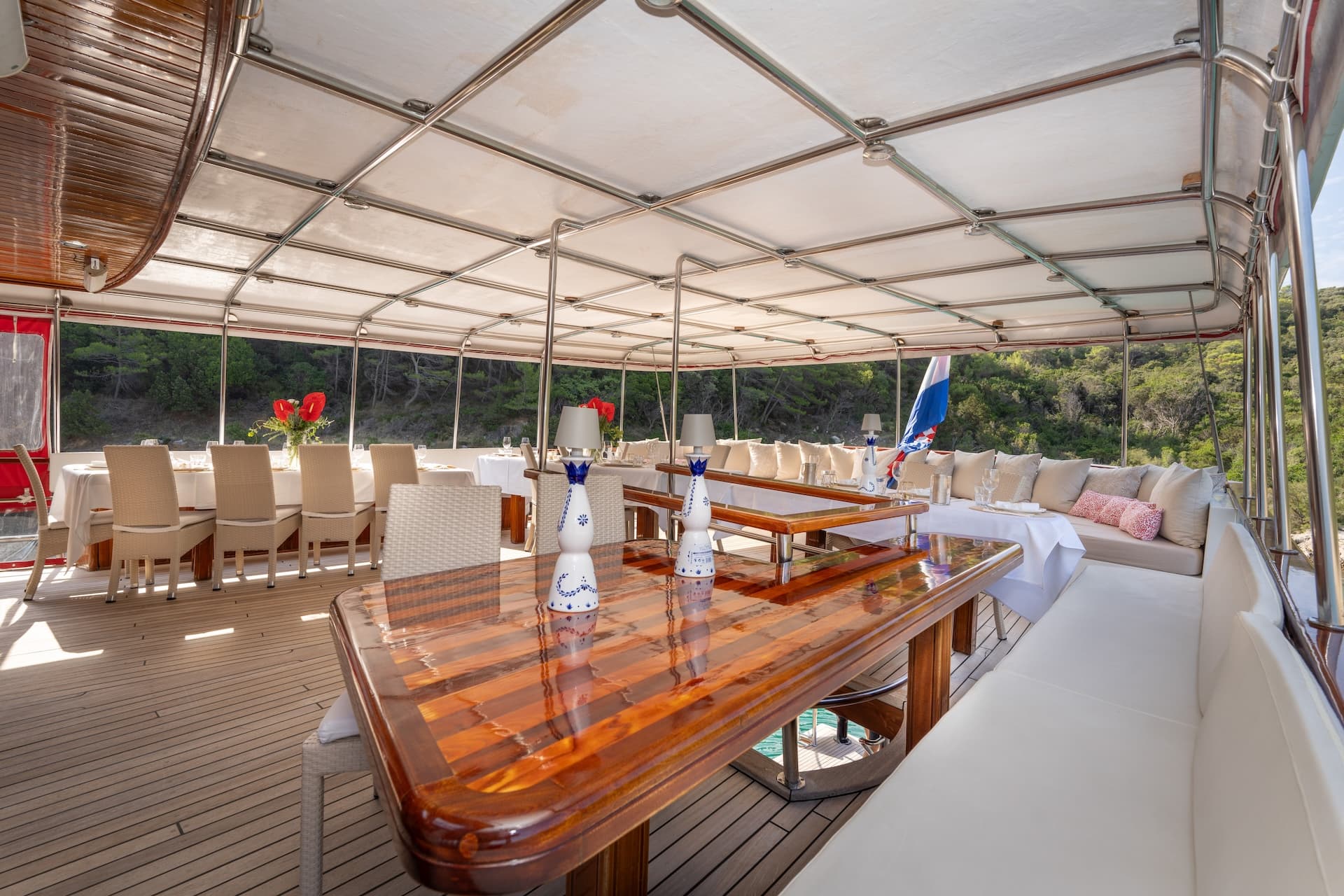 Spacious deck dining area on Gulet Barbara with teak flooring and views of a green coastline.