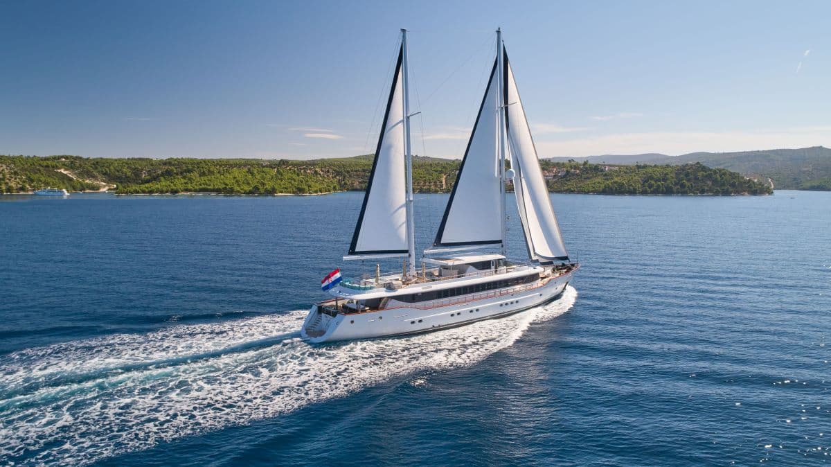 Large white sailing yacht with Croatian flag cruising on deep blue coastal waters.