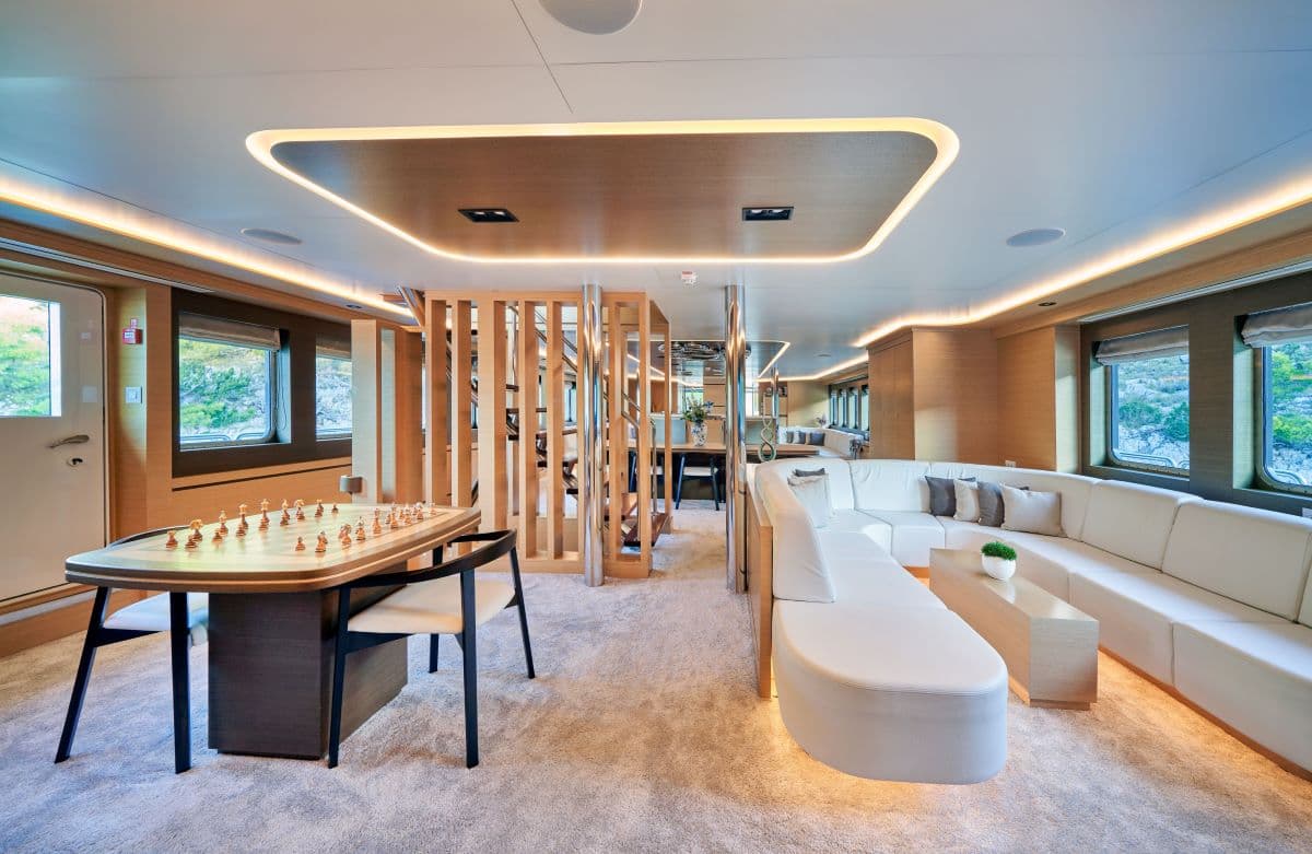 Luxury yacht interior lounge with white sectional sofa, chess table, and wood paneling.