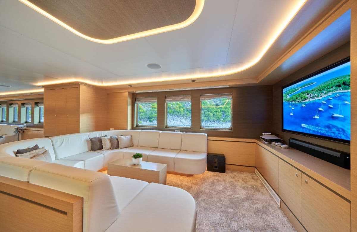 Luxury yacht salon with white leather seating, wood paneling, and ambient lighting, viewing coastline.
