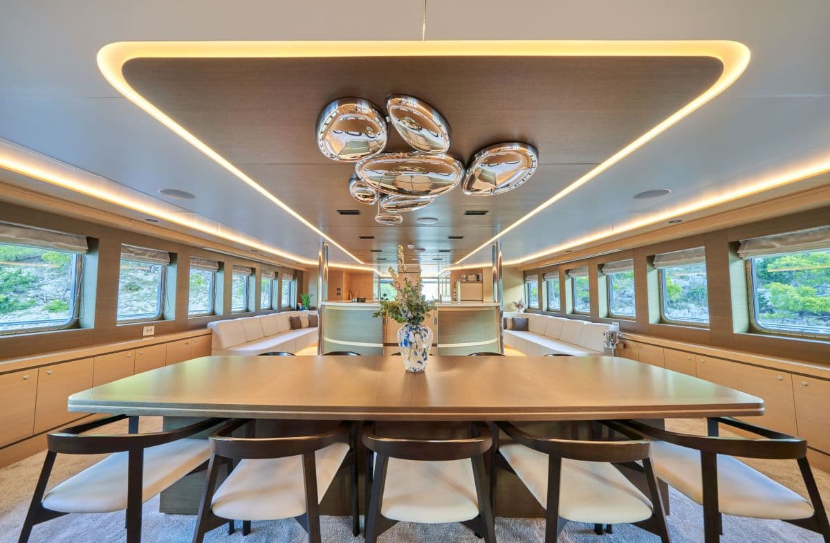 Modern yacht dining area with wood paneling, ambient lighting, and views of green coastline.
