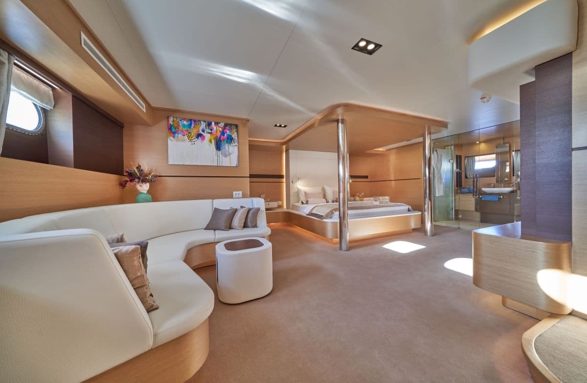 Luxury yacht cabin interior with white curved sofa, wood paneling, and glass-enclosed bathroom.