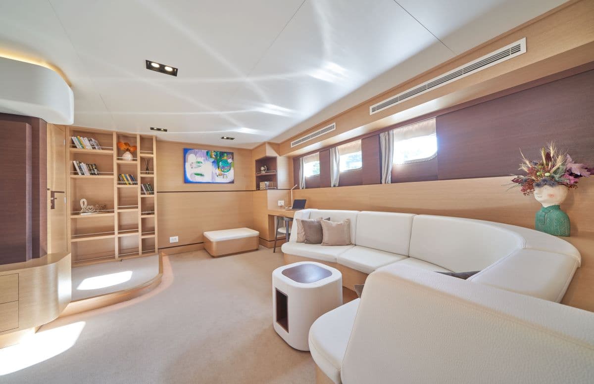 Modern yacht interior lounge with light wood paneling, white curved sofa, and built-in shelving.