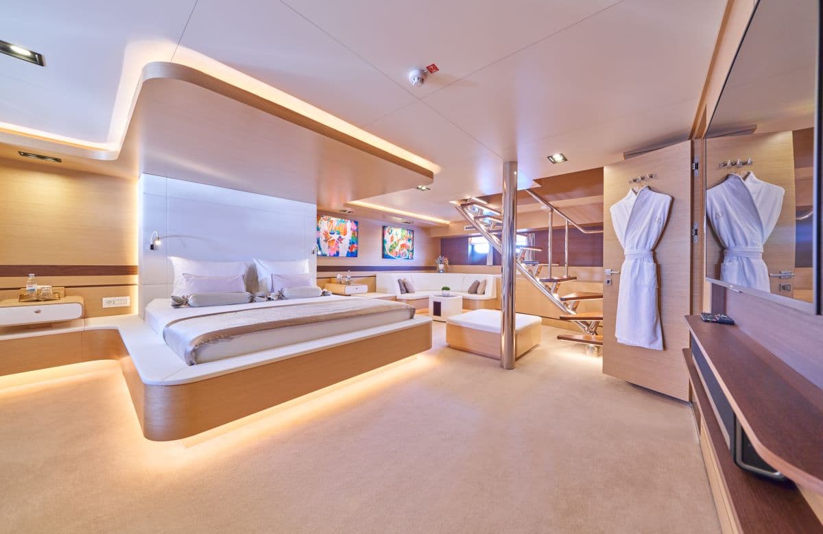 Luxurious yacht cabin with large bed, seating area, and spiral staircase, illuminated interior