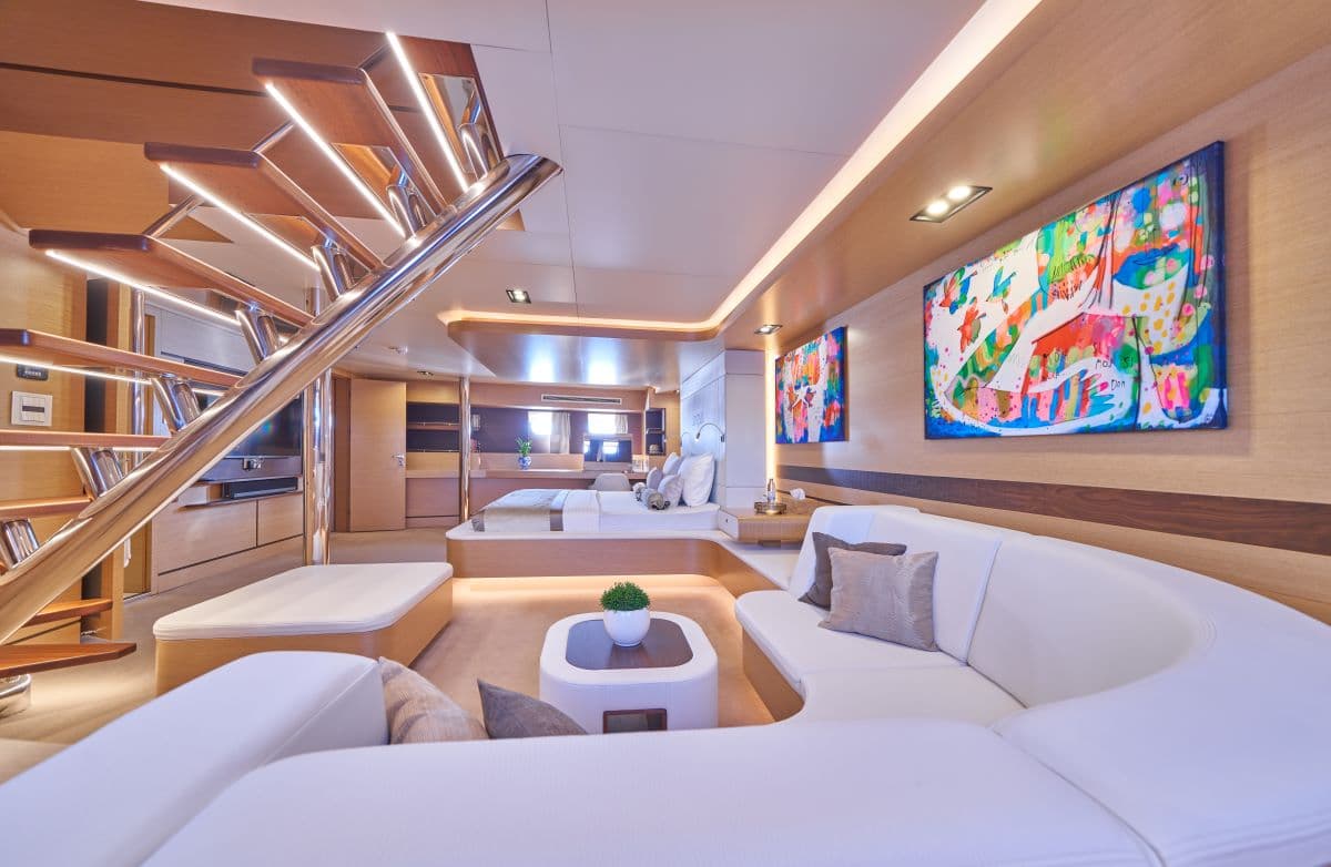 Luxury yacht interior with white seating, wood paneling, illuminated stairs, and colorful abstract art.