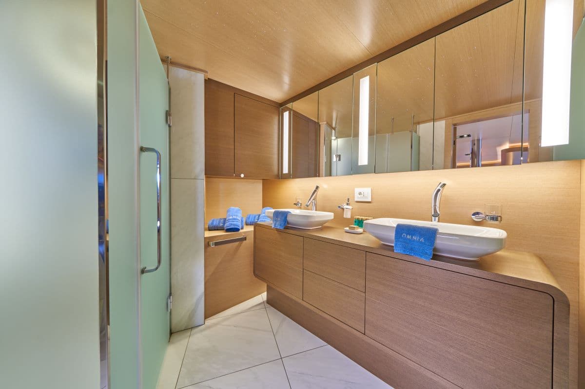 Modern bathroom with double vessel sinks, wood vanity, and frosted glass shower door, likely on a yacht.