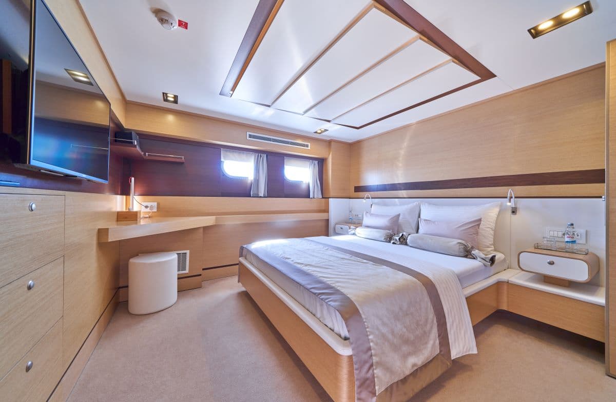 Modern yacht cabin interior with wood paneling, large bed, and flat-screen TV