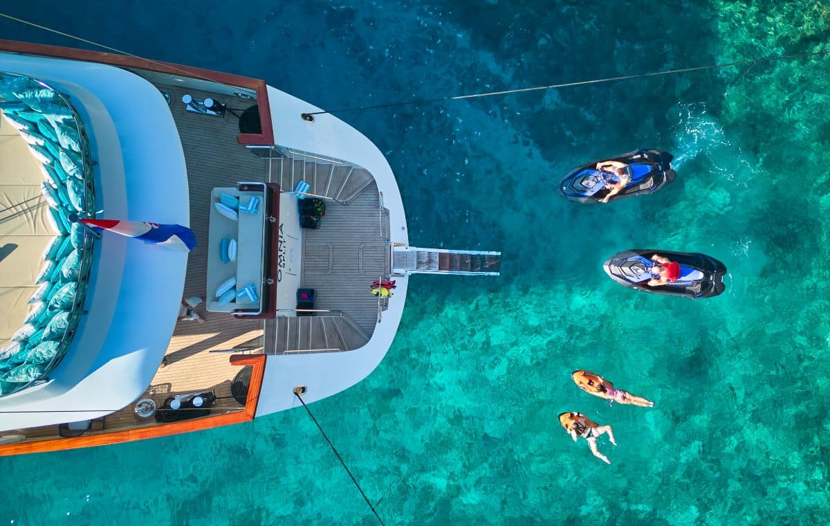 Yacht stern with people jet skiing and swimming in clear turquoise water