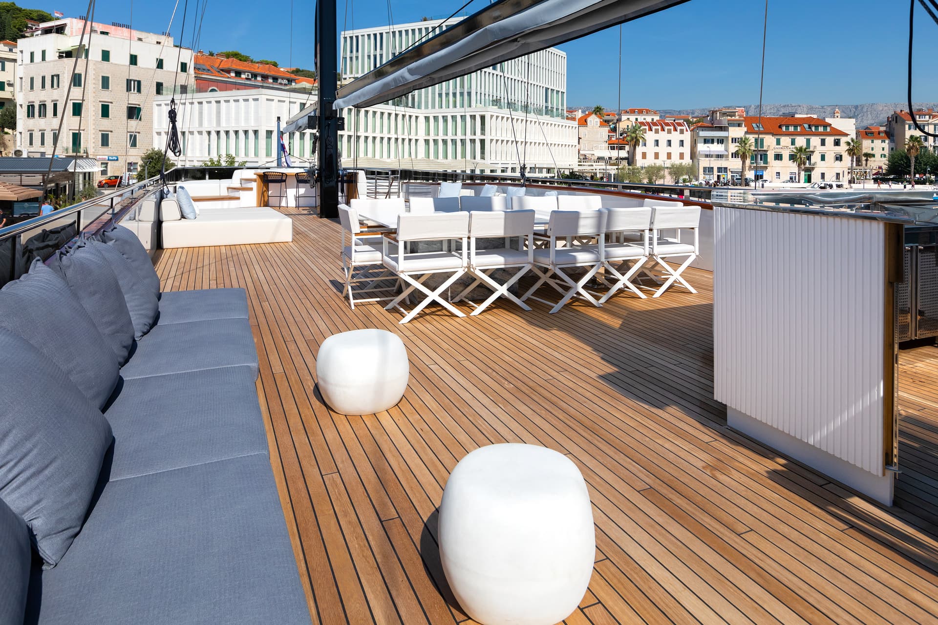 Yacht deck with white seating overlooking coastal city buildings and mountains under blue sky