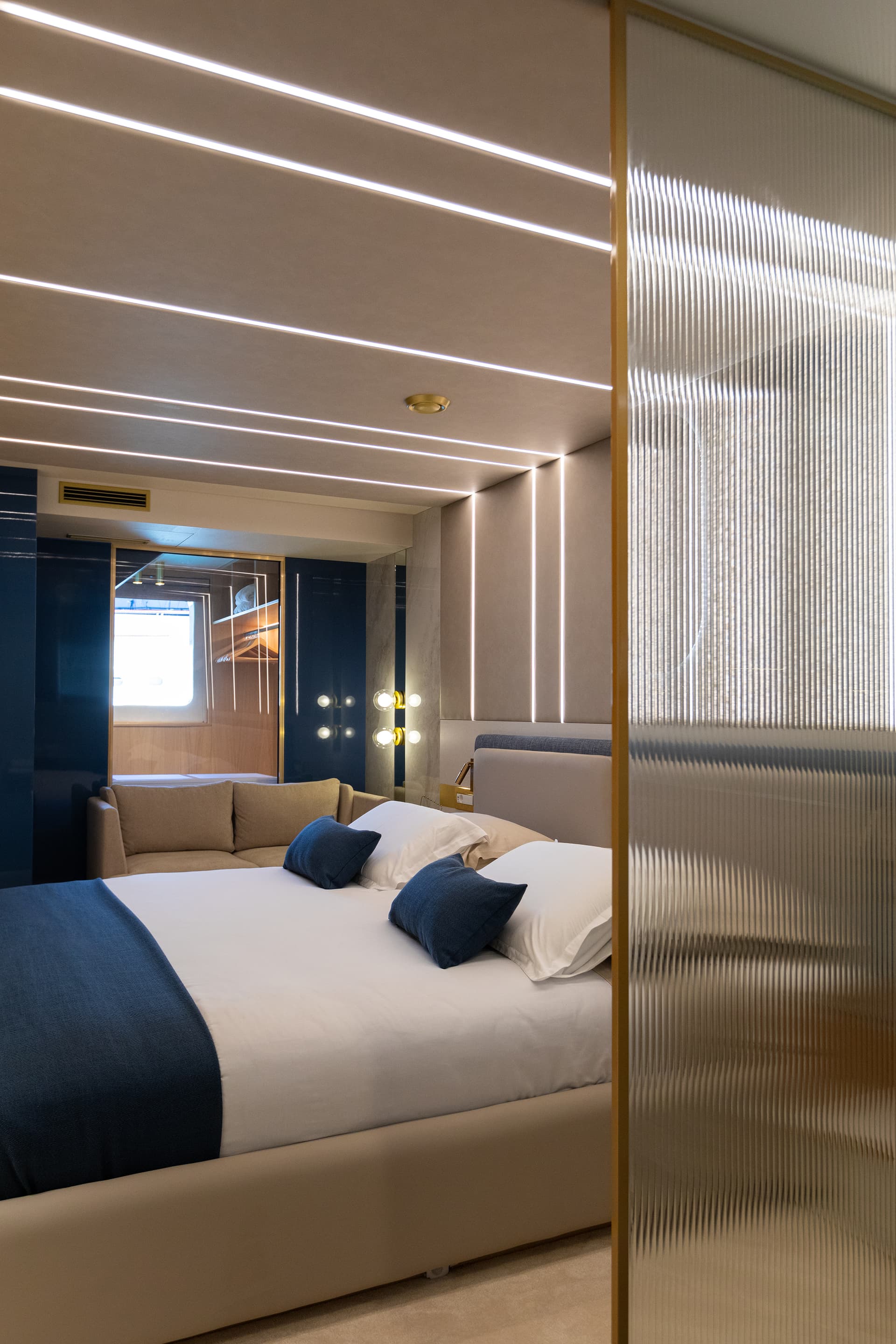 Modern cabin bedroom with built-in lighting, beige bed, and fluted glass partition.