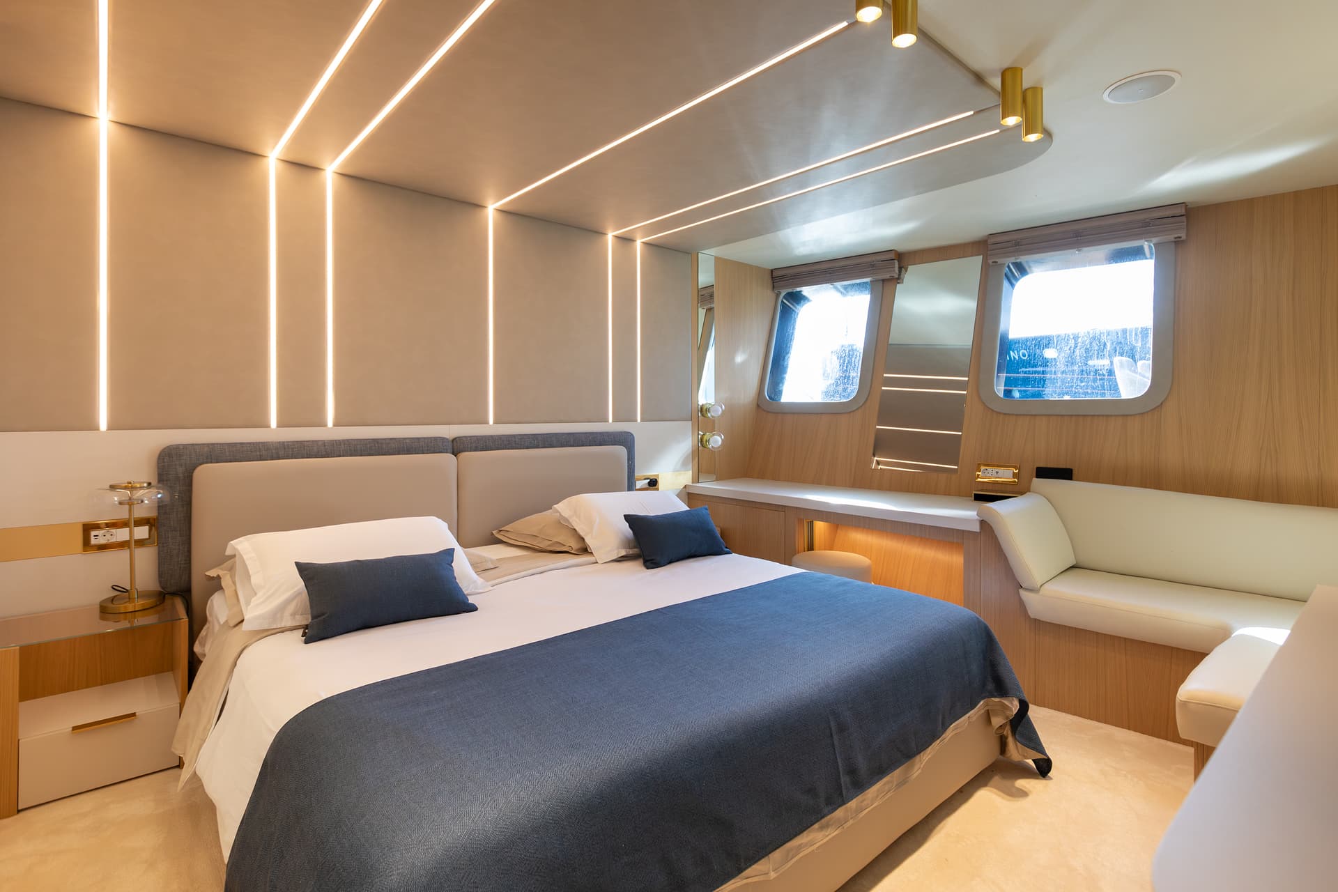 Modern yacht cabin bedroom with illuminated walls, wood paneling, and porthole windows.