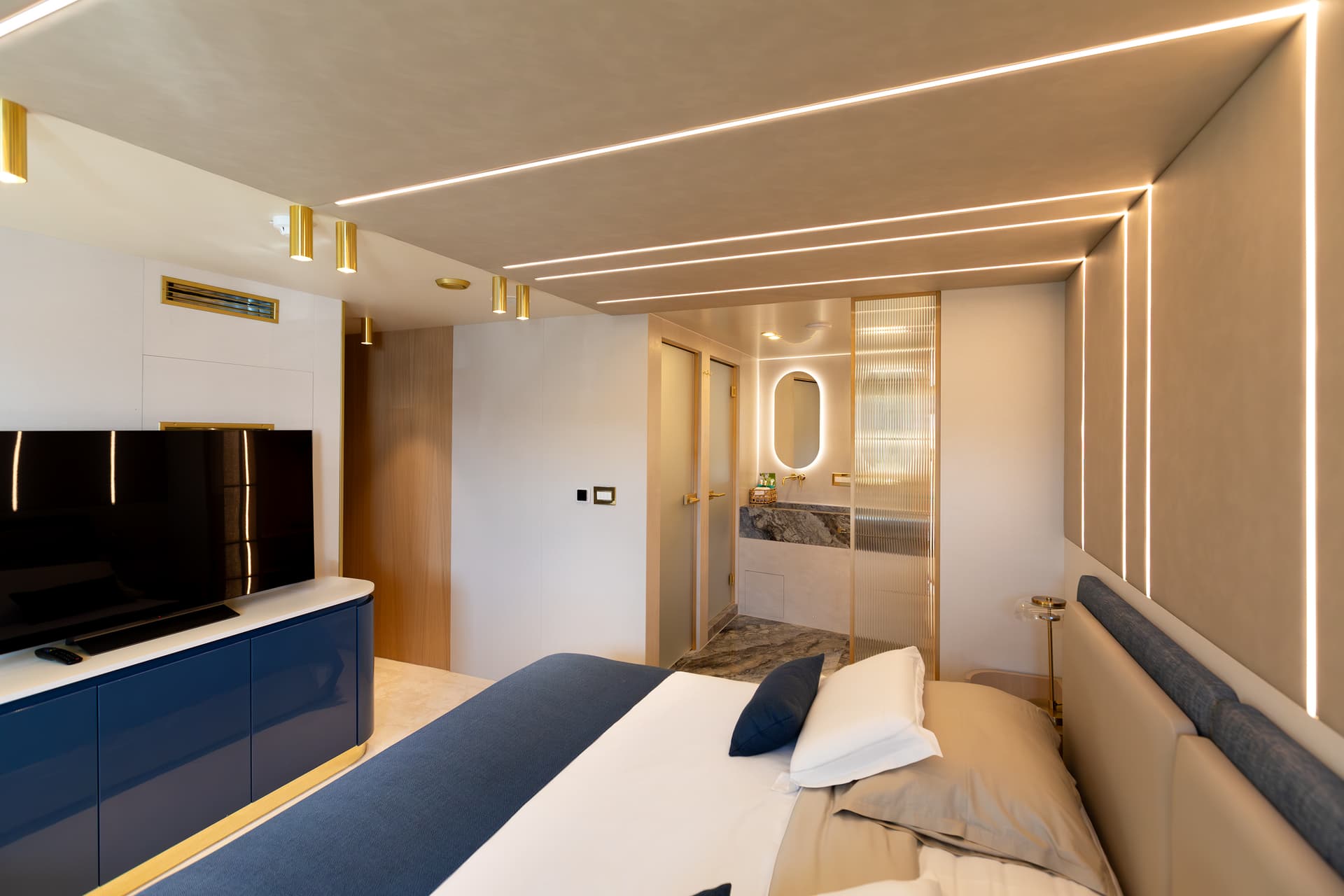 Modern yacht cabin bedroom with integrated lighting, TV, and marble vanity area.