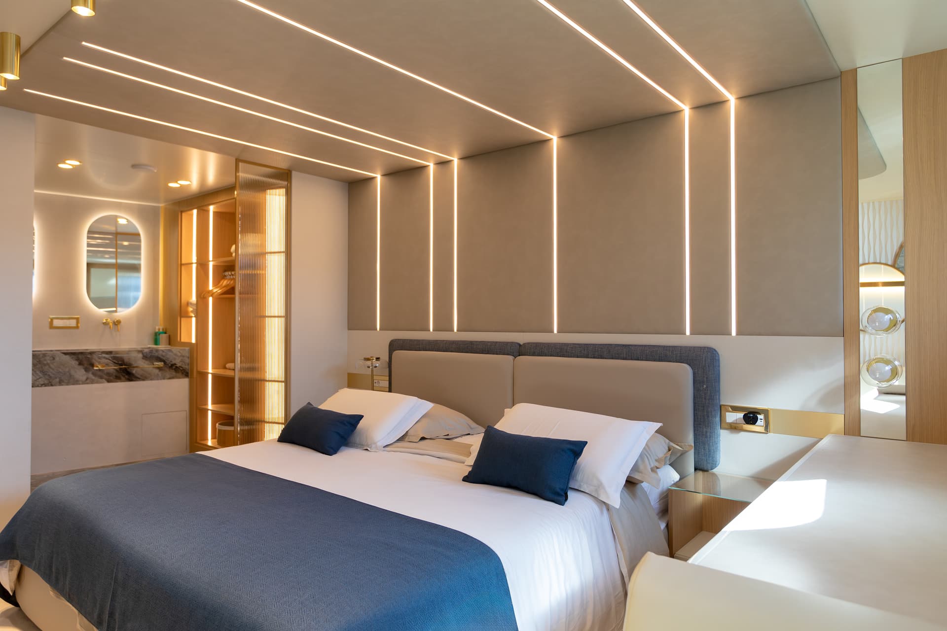 Modern hotel cabin bedroom with illuminated ceiling, blue bedding, and marble vanity area