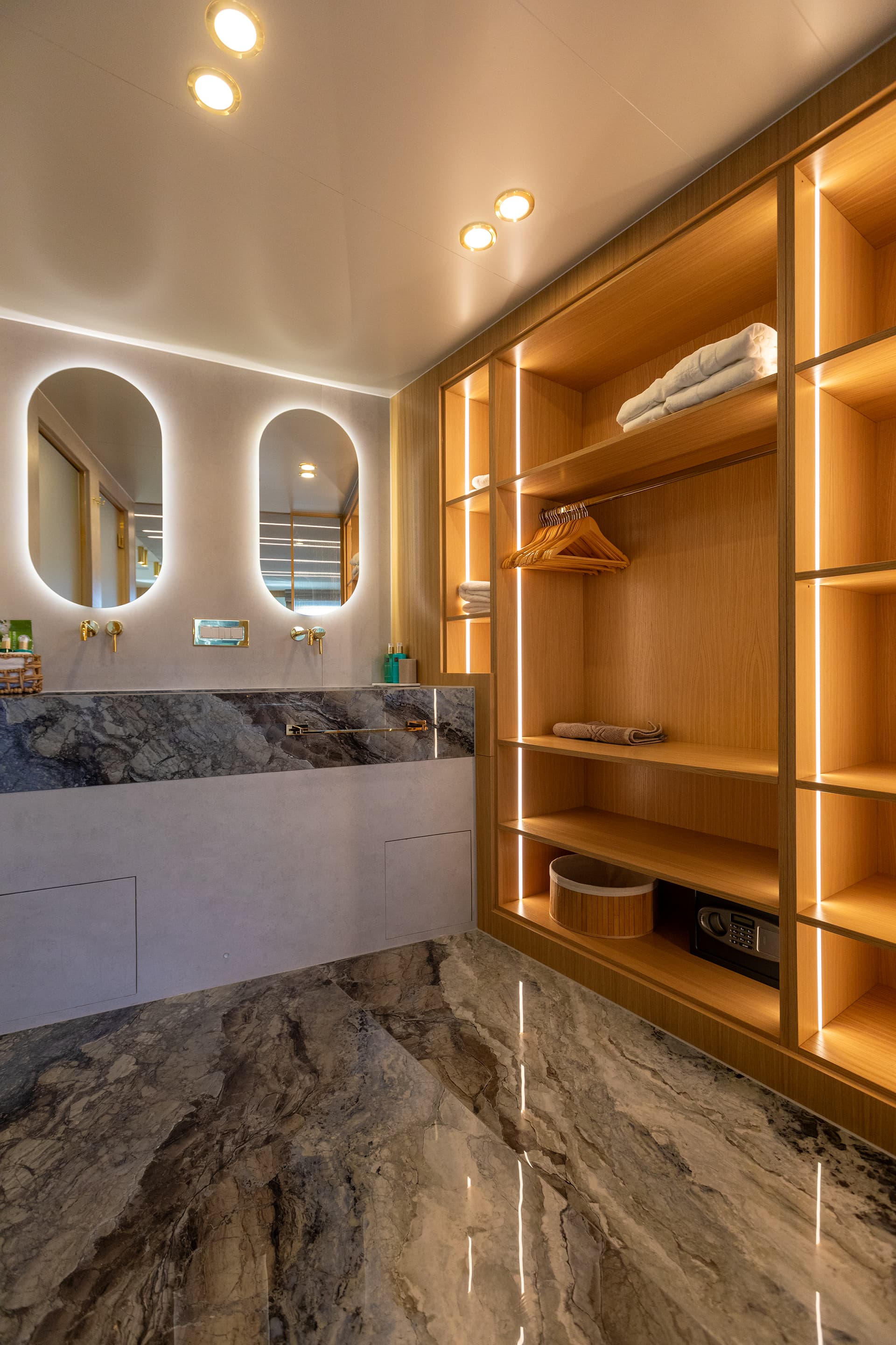 Luxury yacht bathroom with backlit oval mirrors, marble vanity, and illuminated wood shelving with safe.