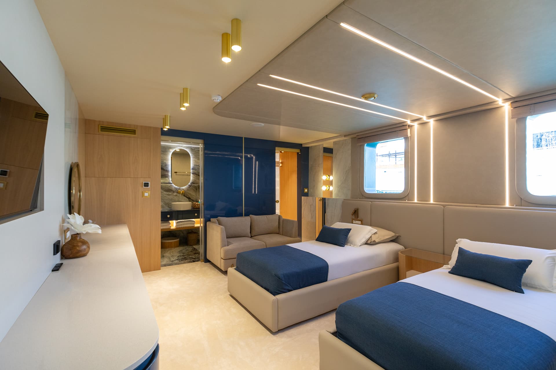 Twin cabin interior with modern lighting, blue accents, and a view of the water through a porthole window.