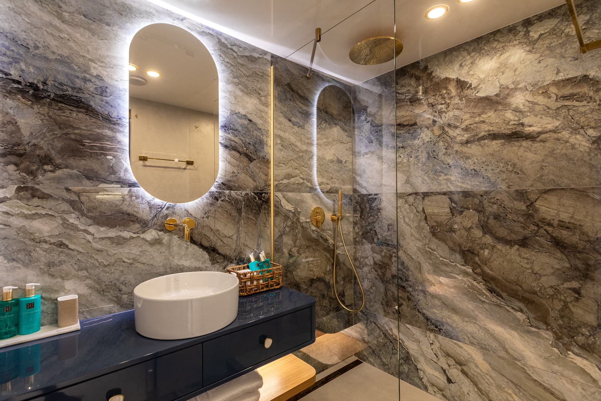 Modern bathroom vanity with vessel sink, backlit mirror, and marble shower enclosure.