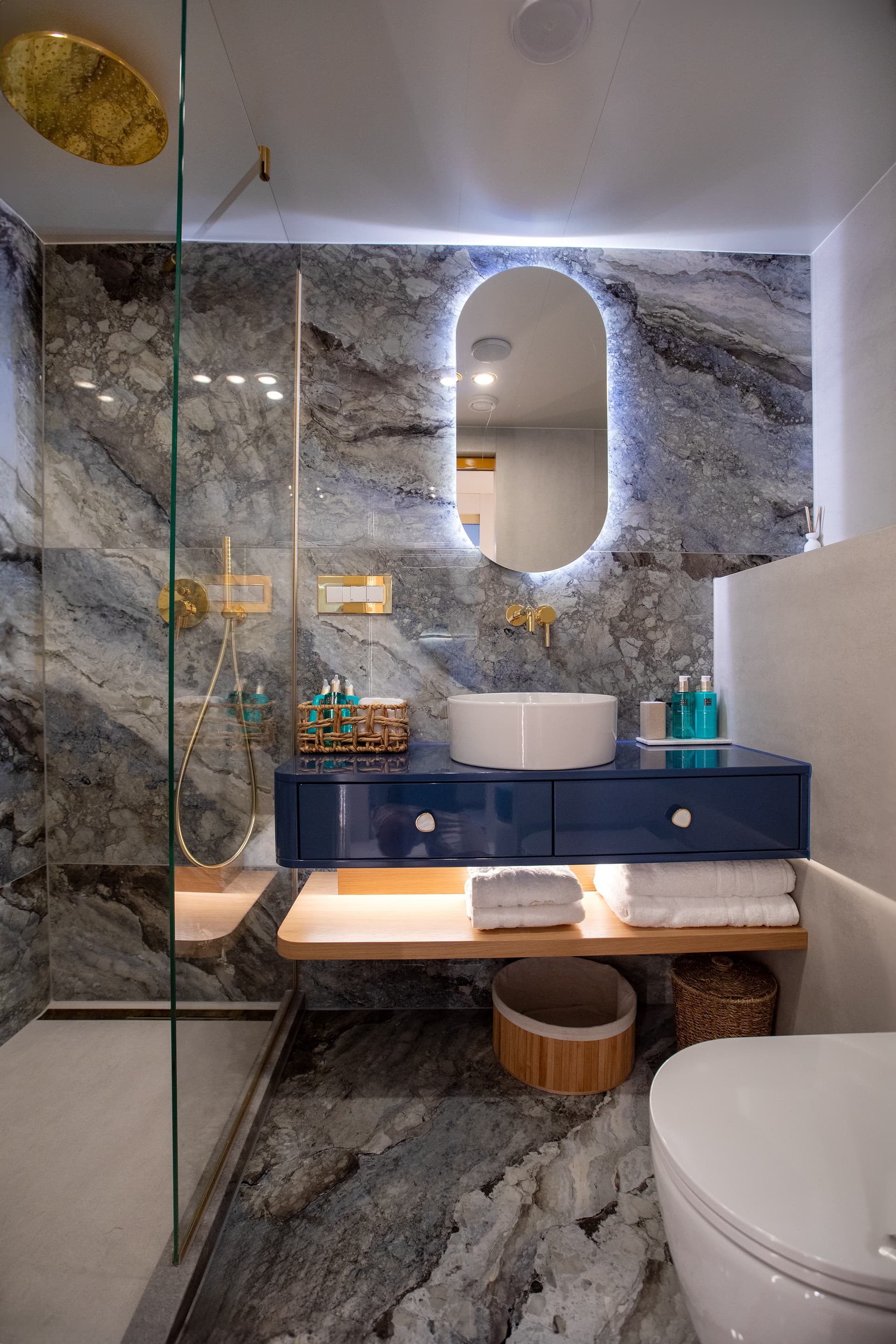Modern bathroom with blue vanity, vessel sink, backlit mirror, and gray marble walls and floor.