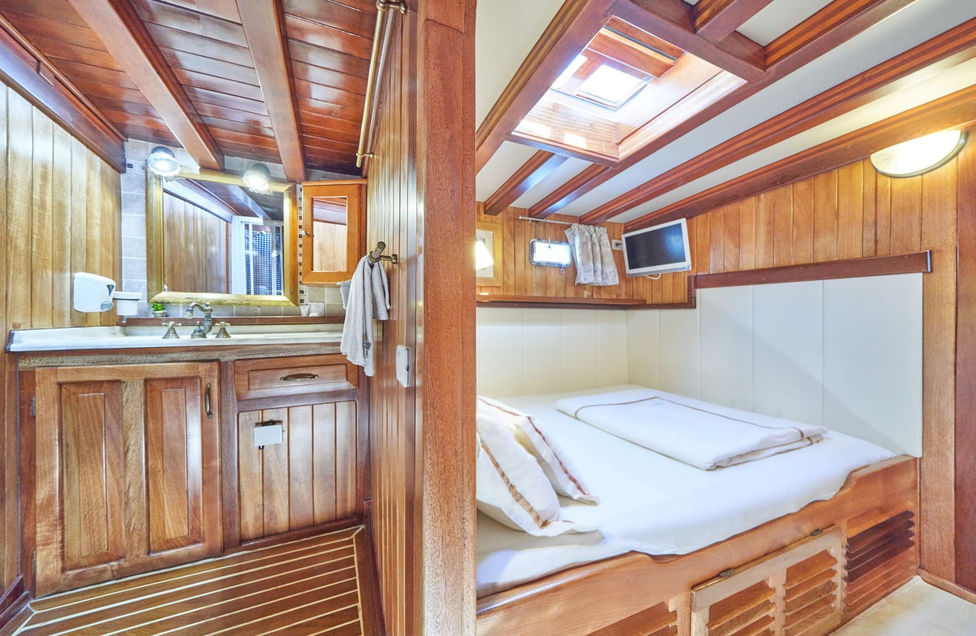 Cabin interior with wood paneling, double bed, vanity, and skylight, likely on a boat