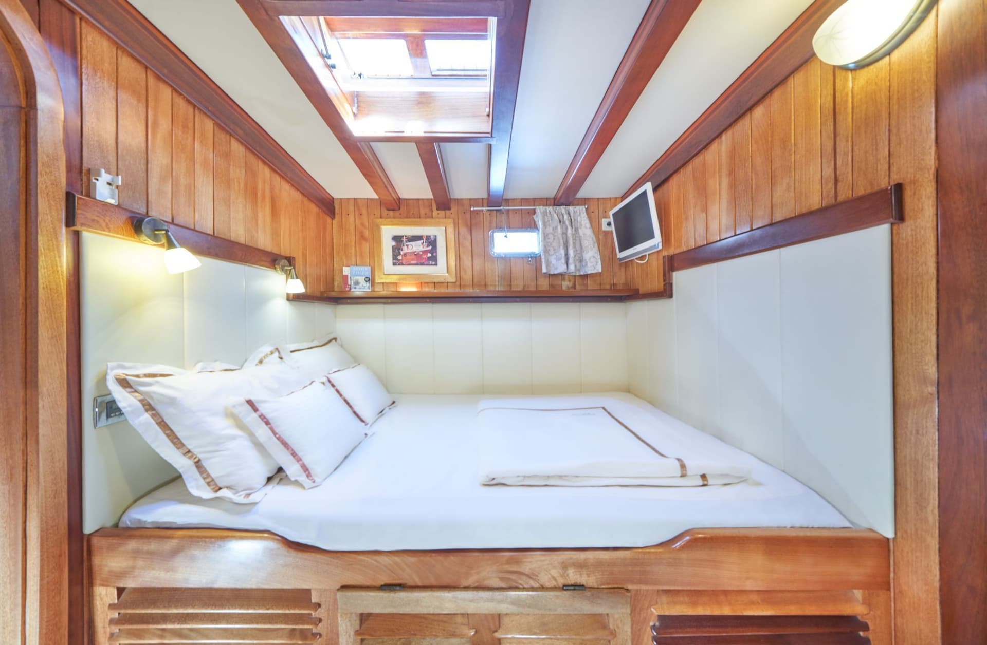 Cozy cabin bedroom with wood paneling, white bedding, and overhead skylight on a boat