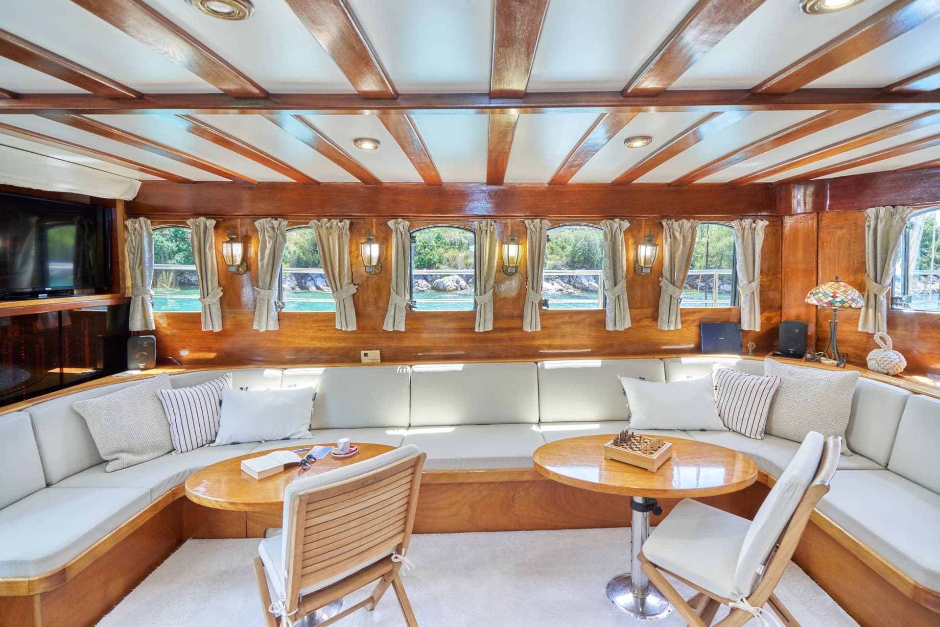 Wood-paneled yacht interior lounge with seating area and view of turquoise water.