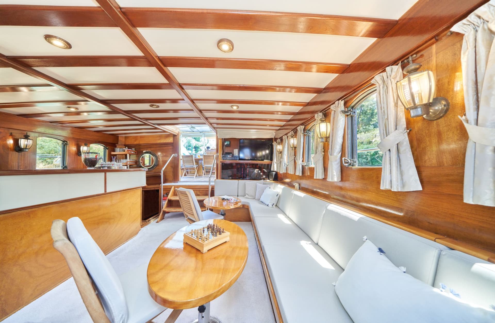 Boat salon interior with wood paneling, white seating, and a chessboard on a table.