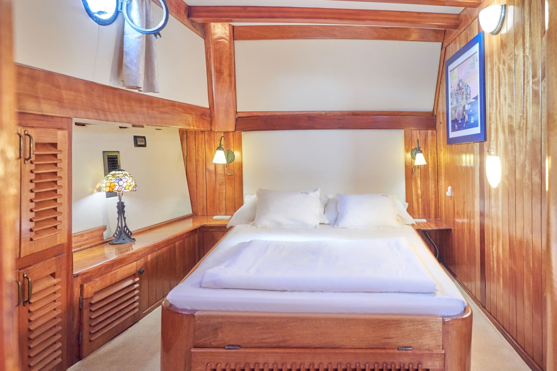 Master cabin bedroom with white bedding and extensive polished wood paneling on boat