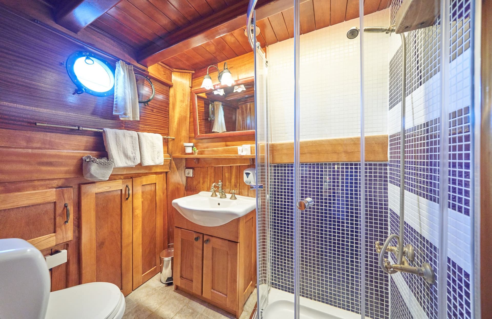 Boat cabin bathroom with wood paneling, white sink, and blue mosaic shower stall.