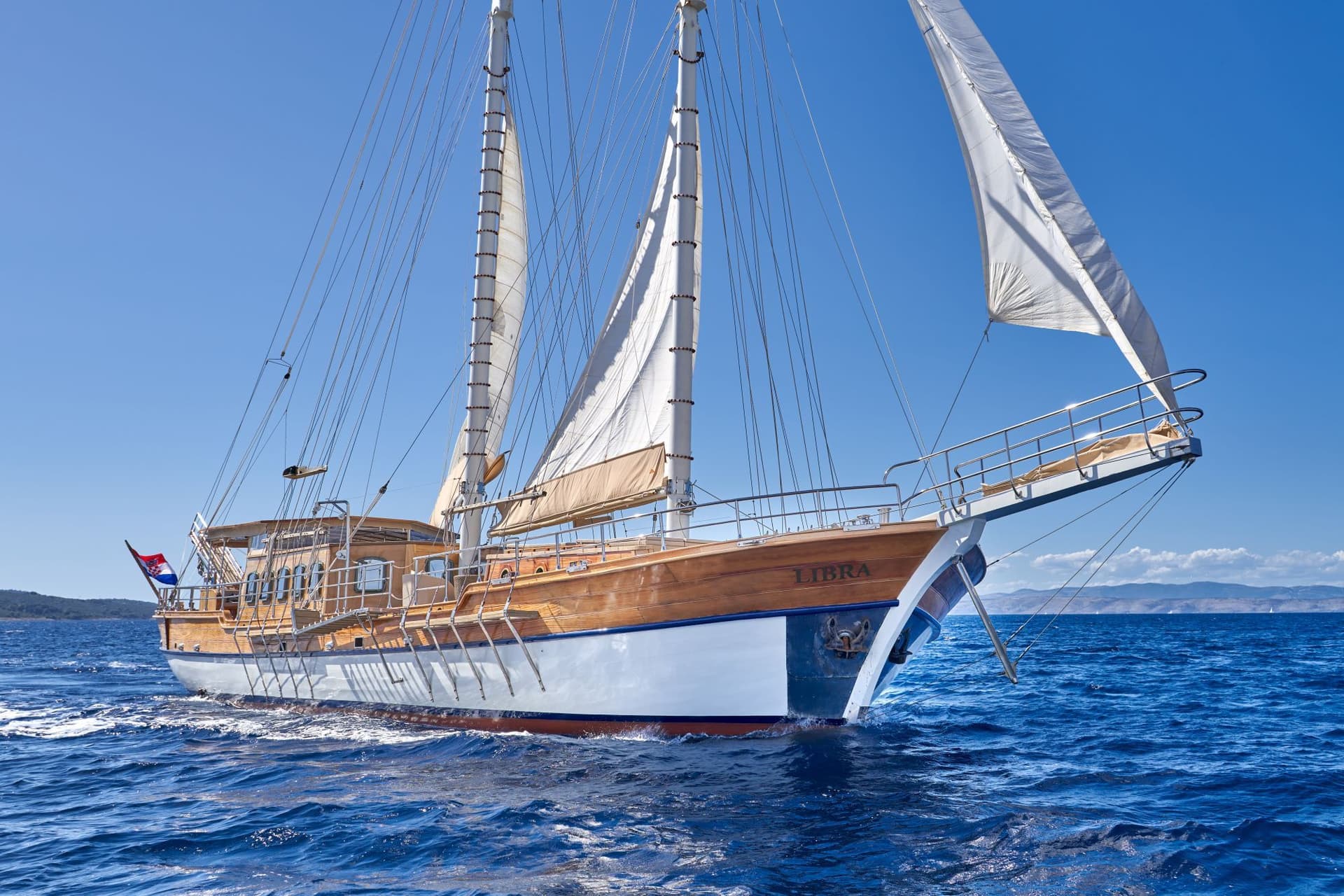 Wooden sailing ship named Libra with sails up on deep blue sea near coastline.