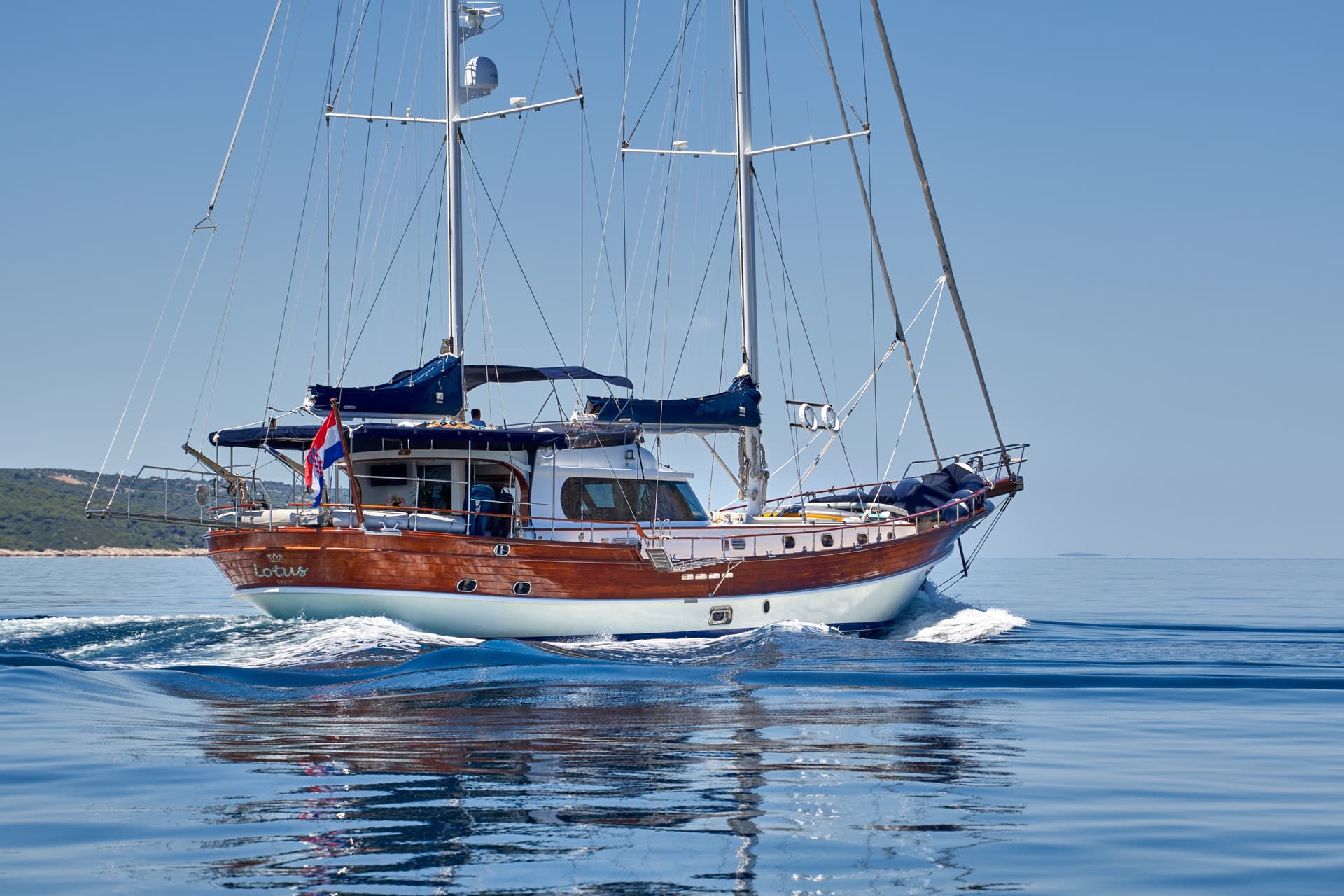 Wooden sailboat named Lotus from Split cruising on calm blue sea near coastline