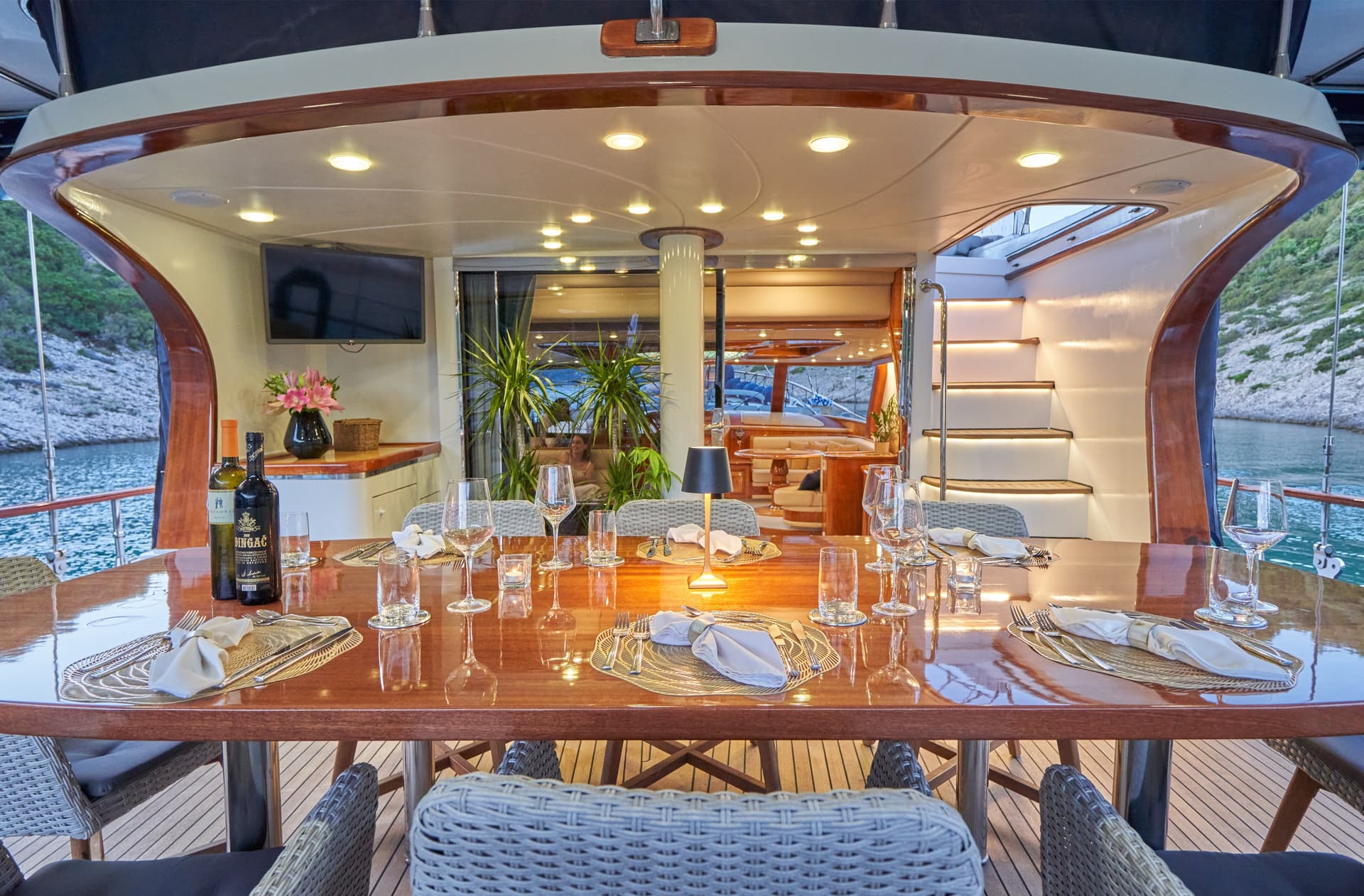 Dining table set for dinner on a yacht anchored near a rocky coastline.